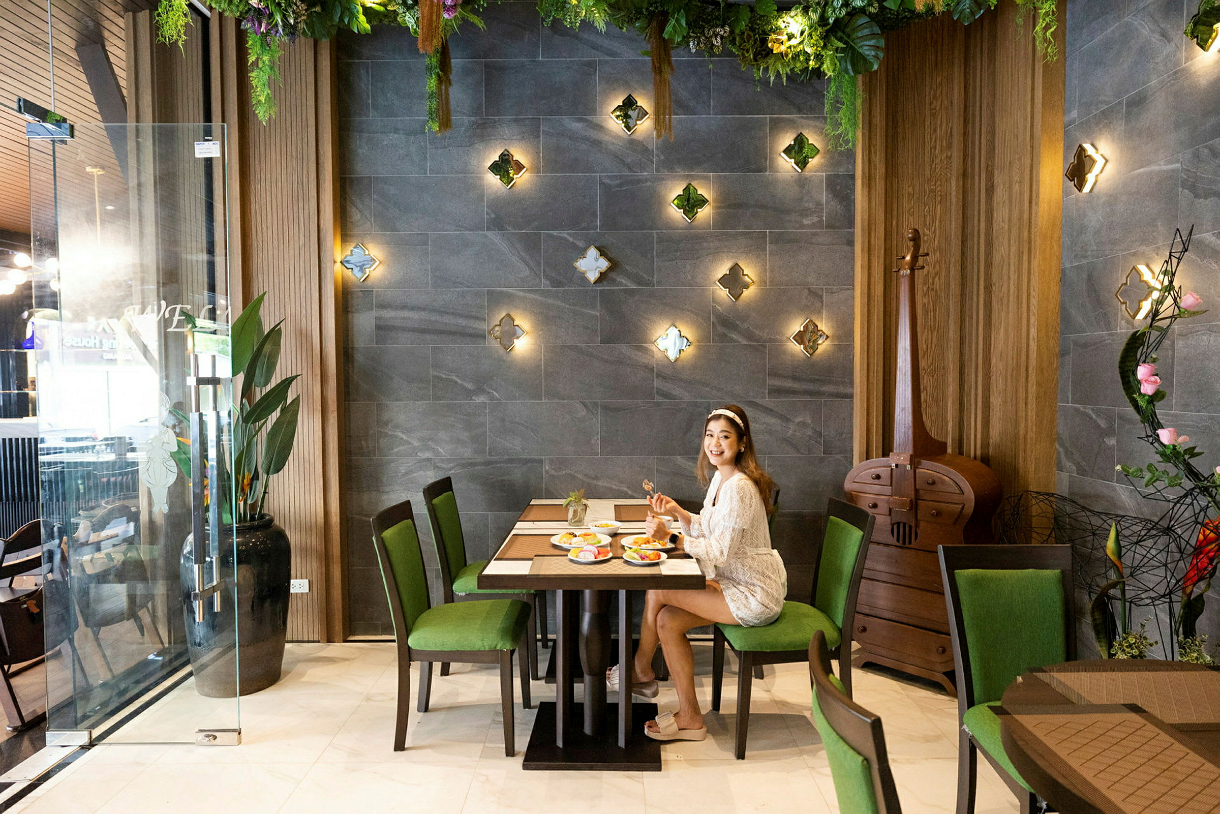 Person sidder ved et bord på en restaurant med vægdekorationer og frodigt interiør. (AI-genereret tekst)