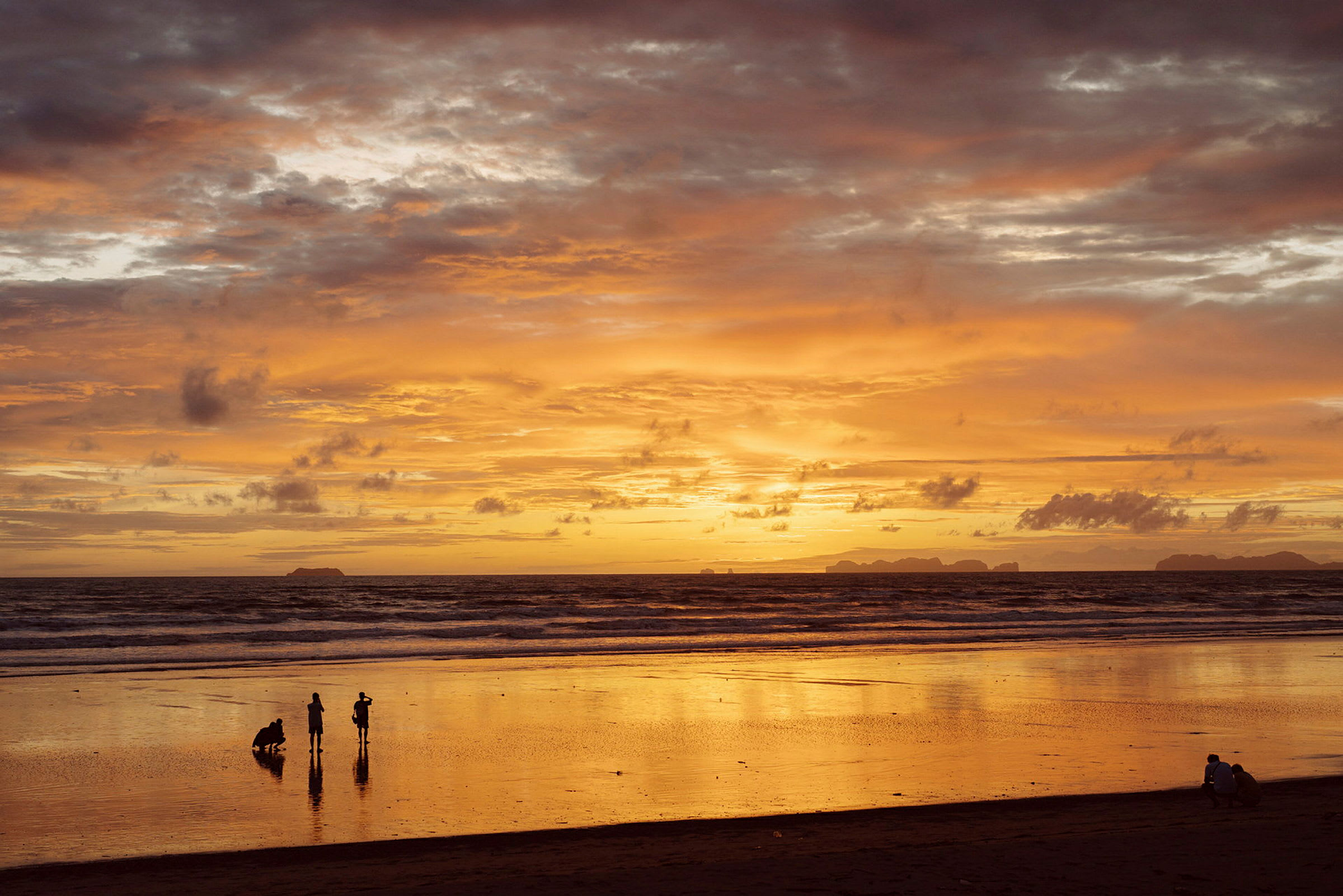 En strand ved solnedgang med nogle mennesker, der står ved vandet. (AI-genereret tekst)