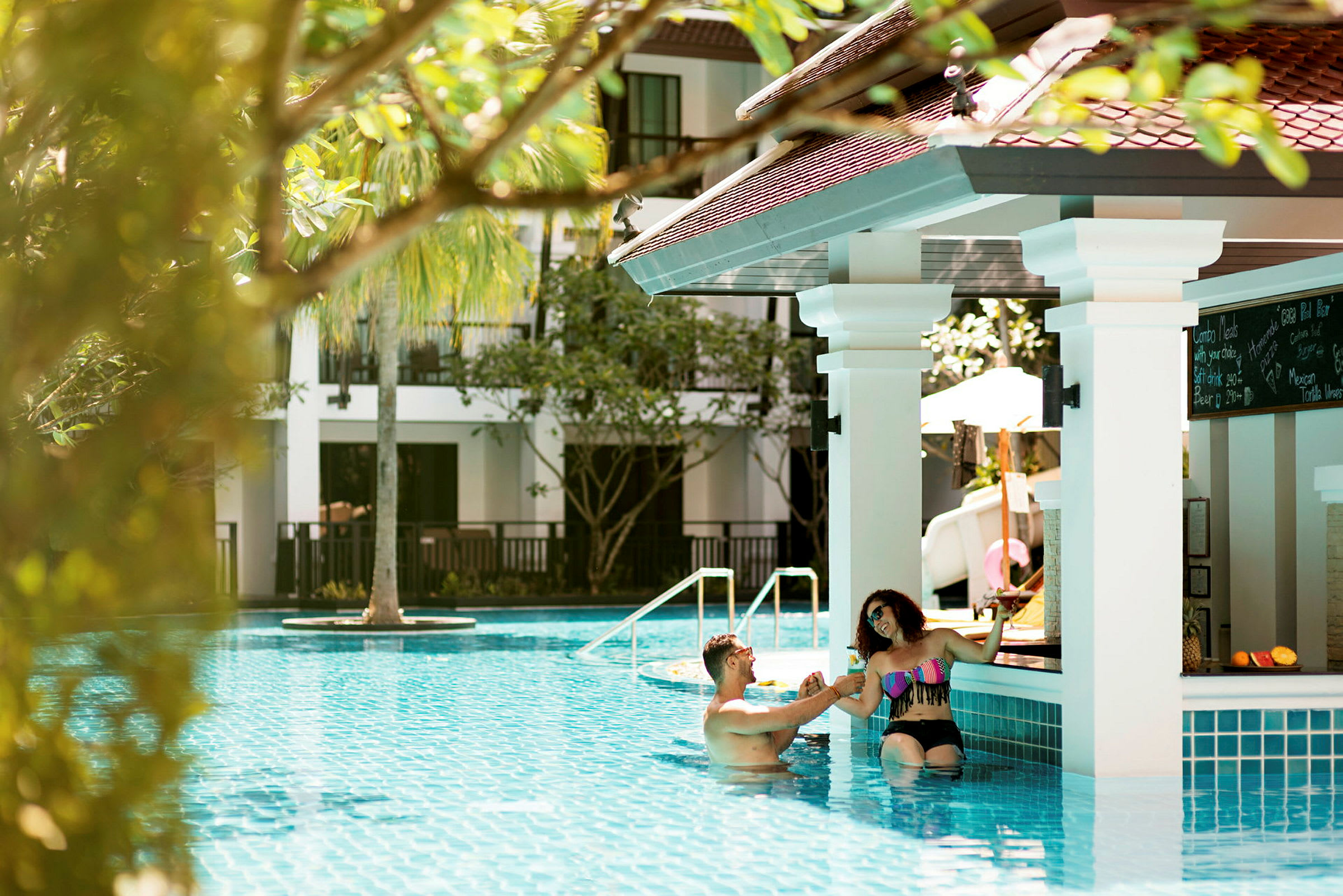 To personer i en pool ved siden af en poolbar på et solrigt resort. (AI-genereret tekst)