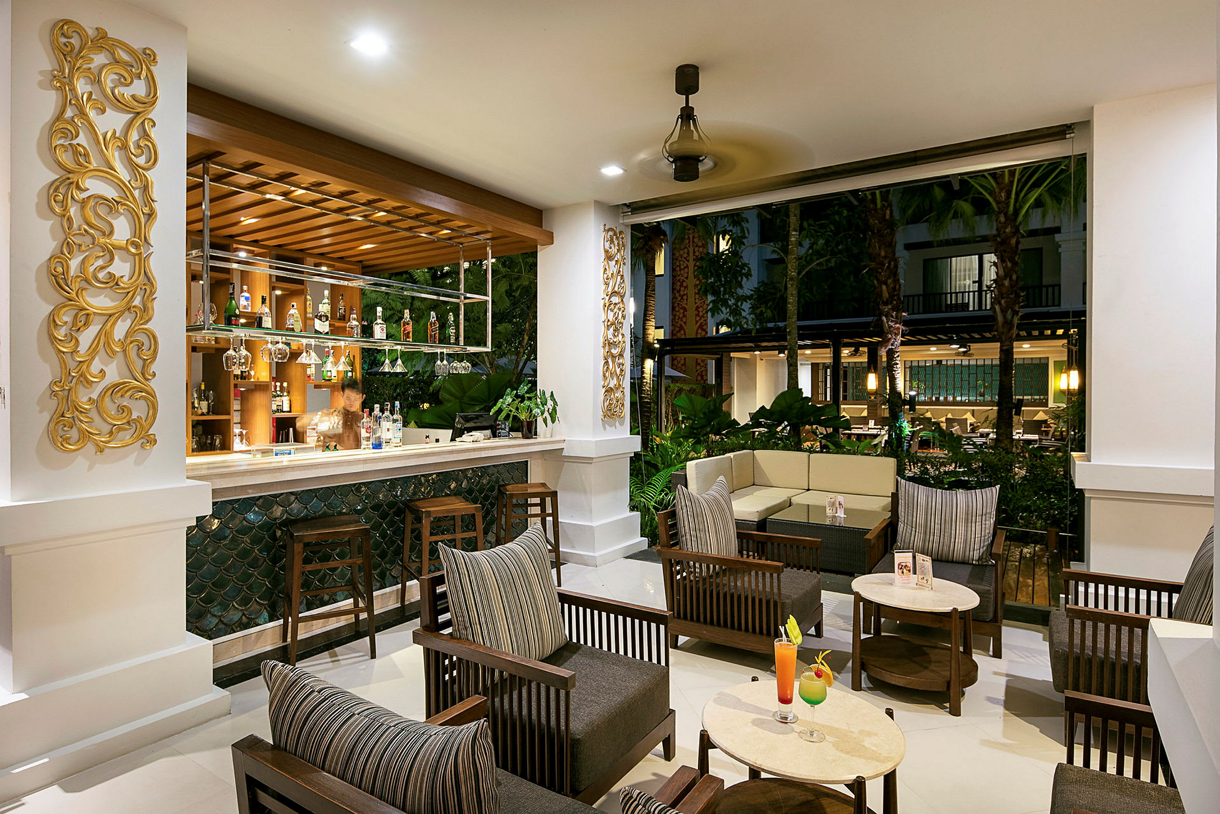Et elegant og veloplyst loungeområde med en bar, siddegrupper og udsigt over et frodigt udemiljø. (AI-genereret tekst)
