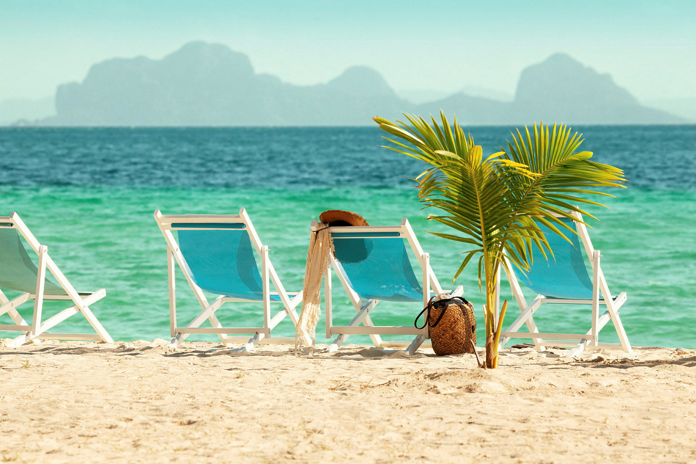 Solsenge på sandstrand med palme og hav i baggrunden. (AI-genereret tekst)