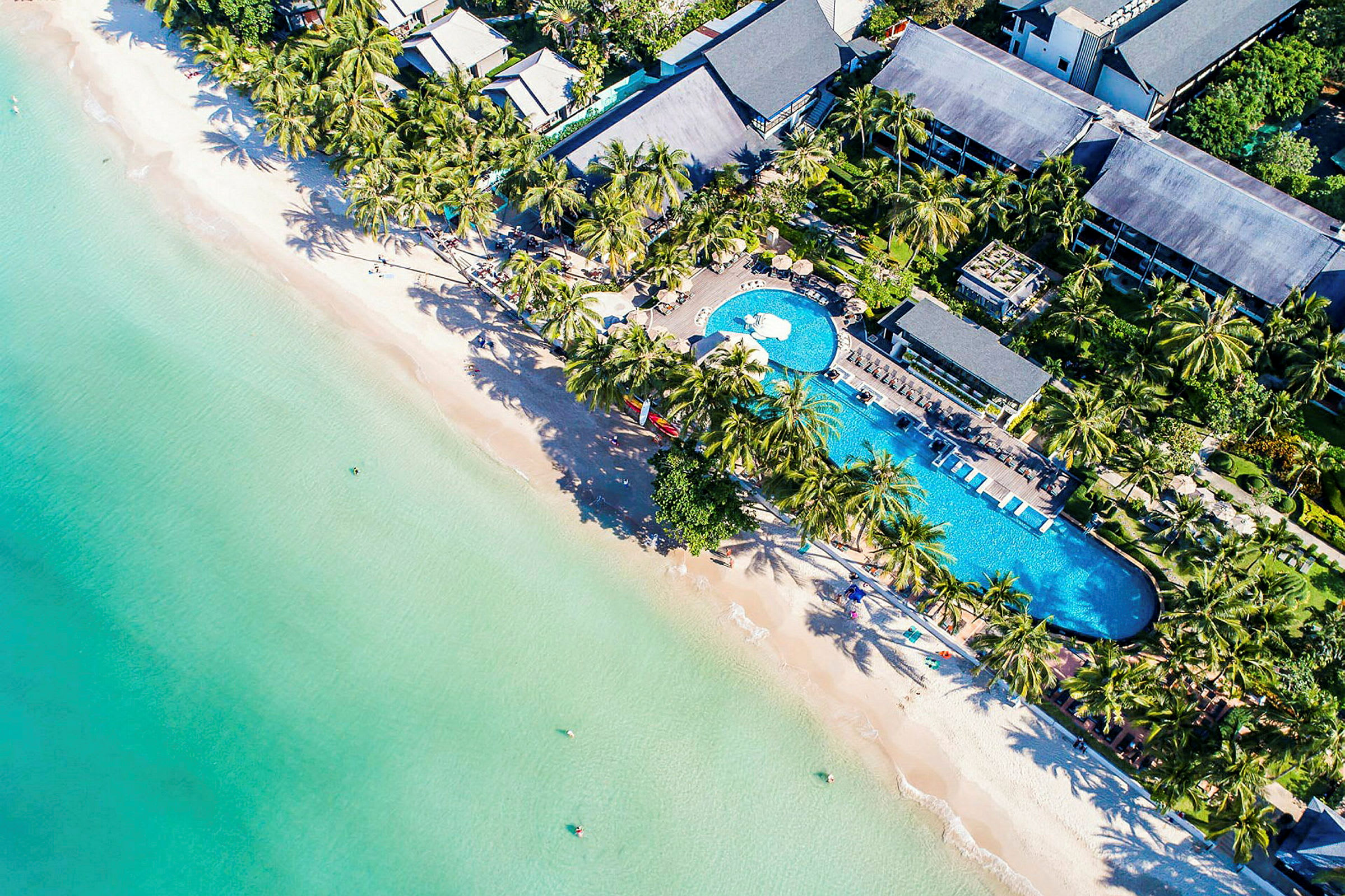 Luftfoto af en resort ved stranden med swimmingpool, palmer og bygninger. (AI-genereret tekst)
