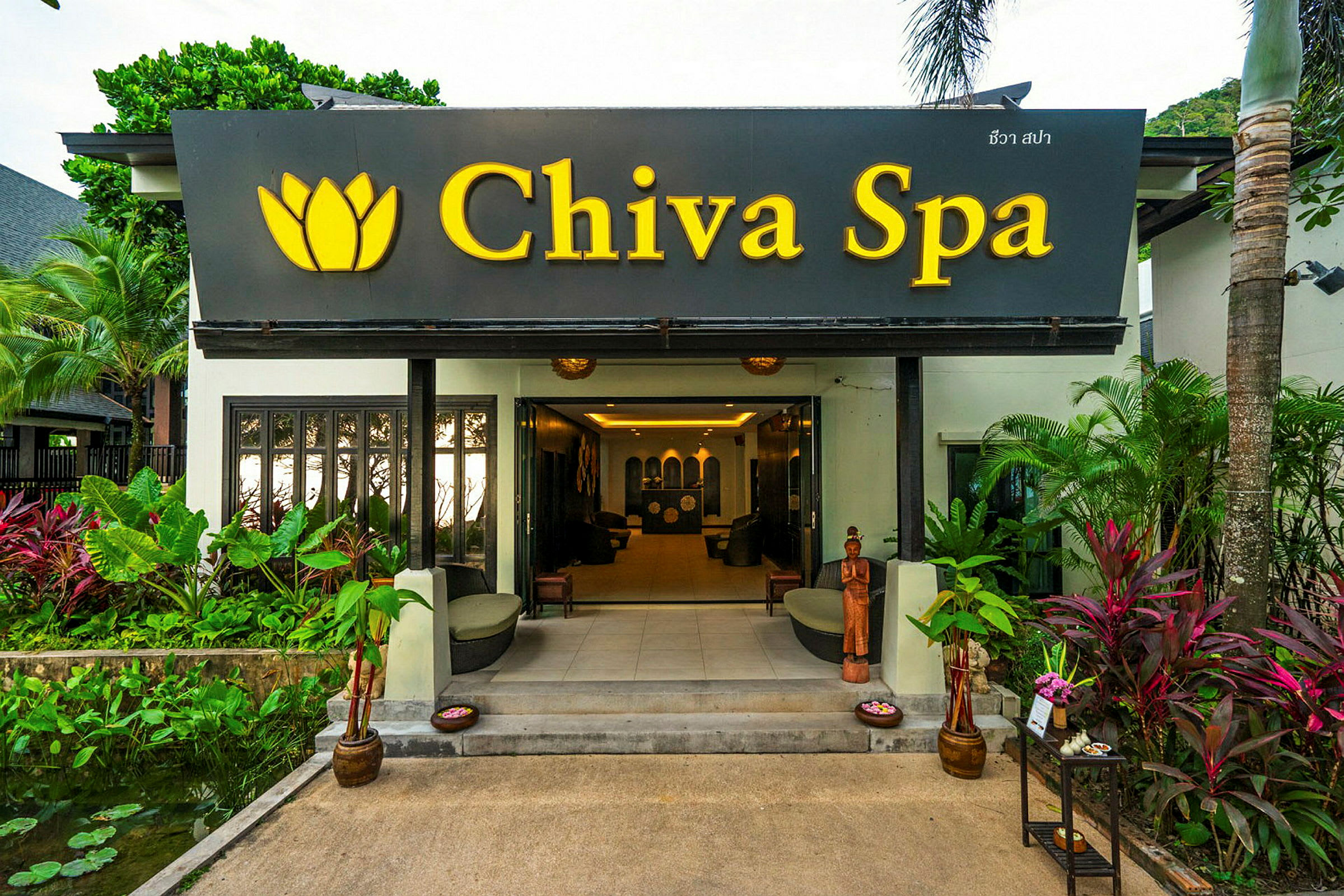 Indgangen til et spa-anlæg med skiltet "Chiva Spa" og omkringliggende planter. (AI-genereret tekst)
