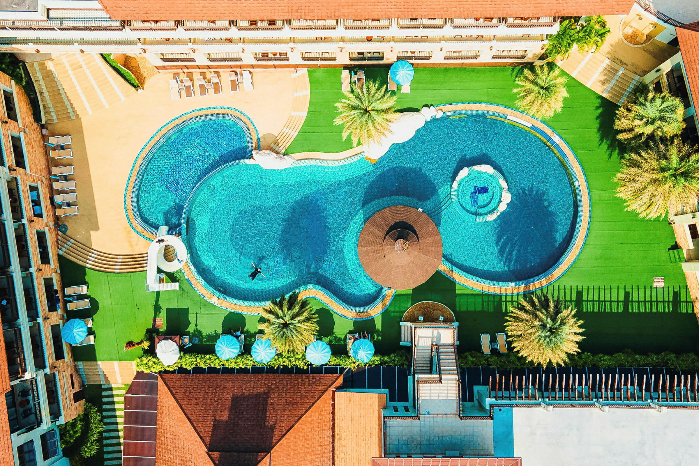 Luftfoto af en hotelpool omgivet af liggestole og frodige områder. (AI-genereret tekst)