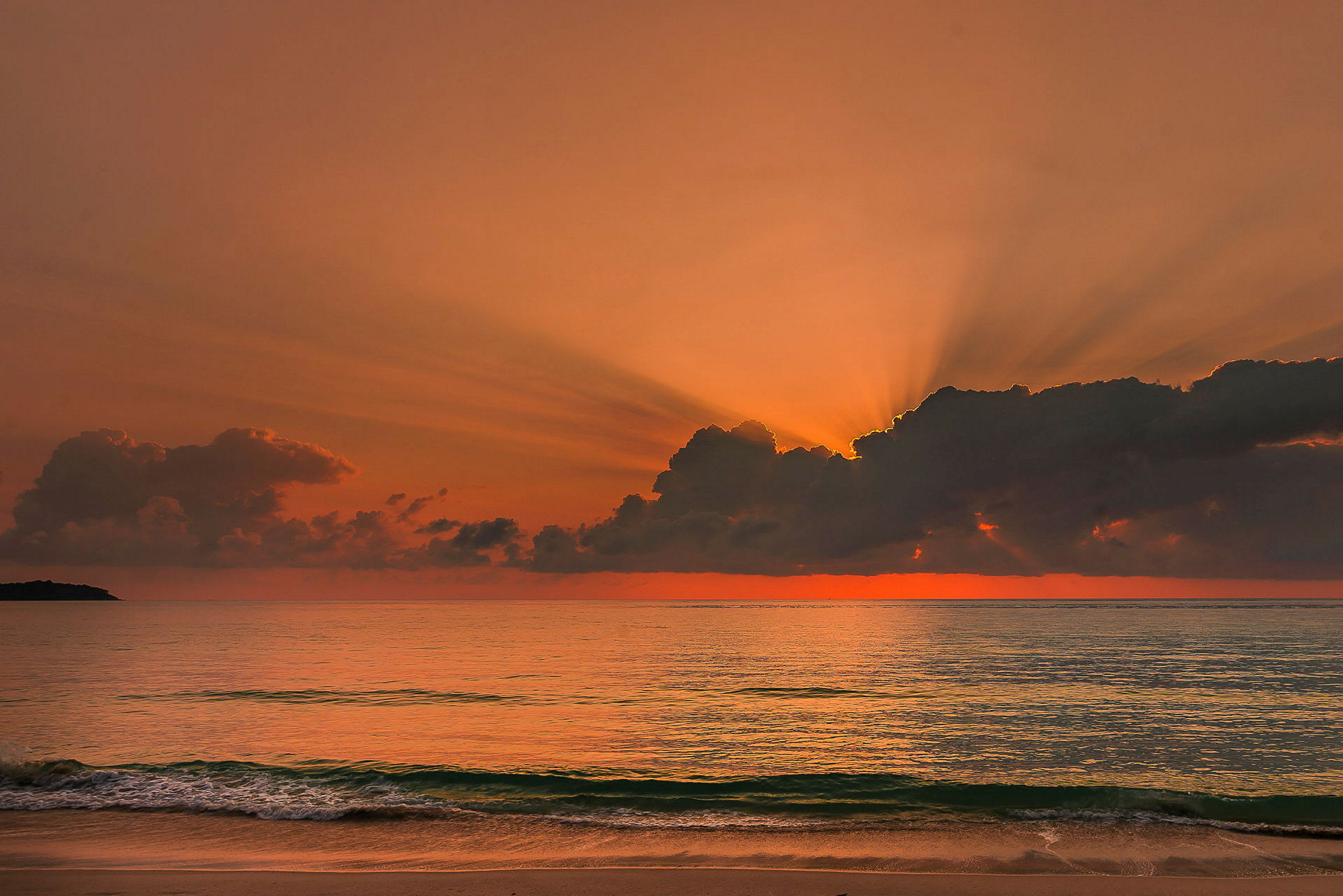 En solnedgang over havet, hvor røde og orange farver lyser op i skyerne, med bølger som ruller ind mod stranden i forgrunden. (AI-genereret tekst)