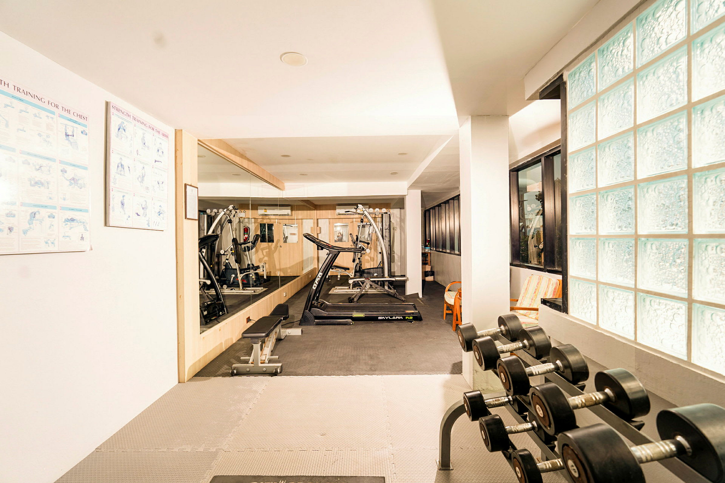 Et fitnesscenter med træningsudstyr som løbebånd, bænkpres og håndvægte i et lyst lokale. (AI-genereret tekst)