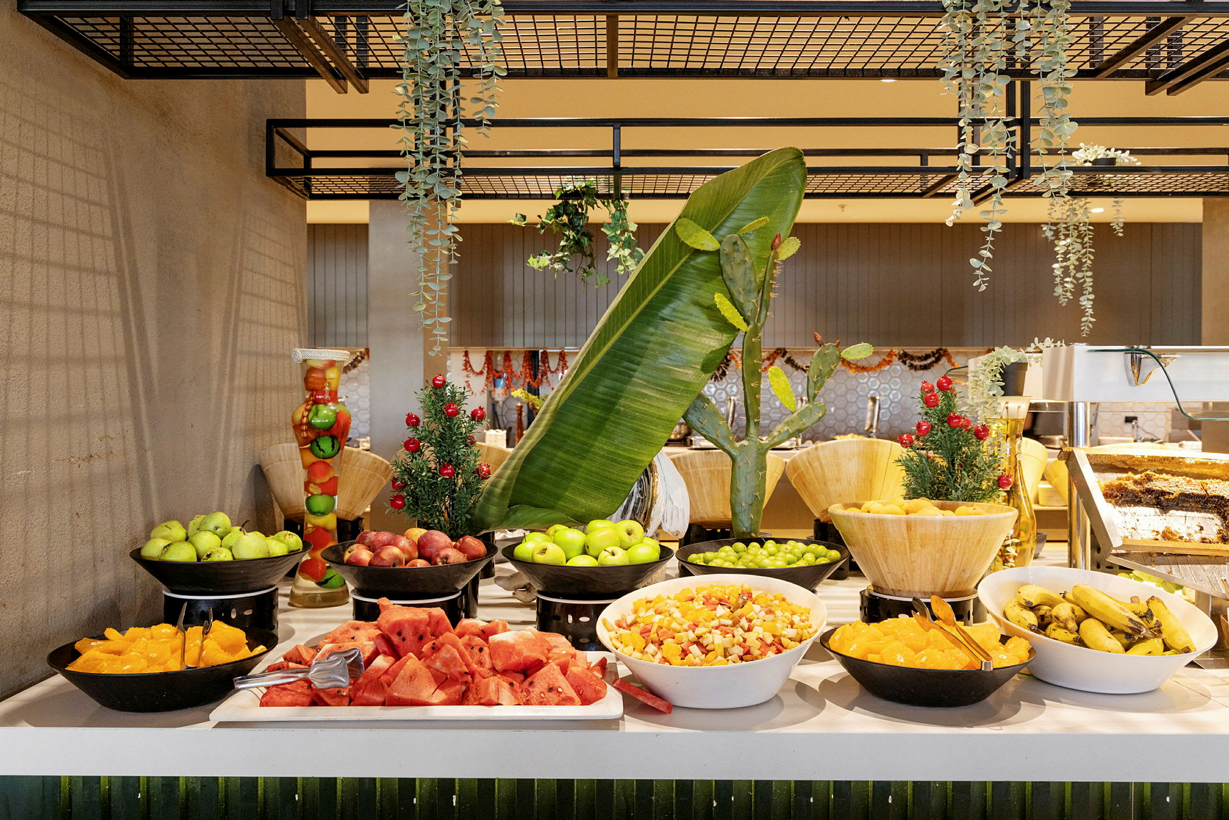 En buffet med forskellige frugter, herunder vandmelon, bananer og skåret frugtsalat, dekoreret med grønne blade. (AI-genereret tekst)