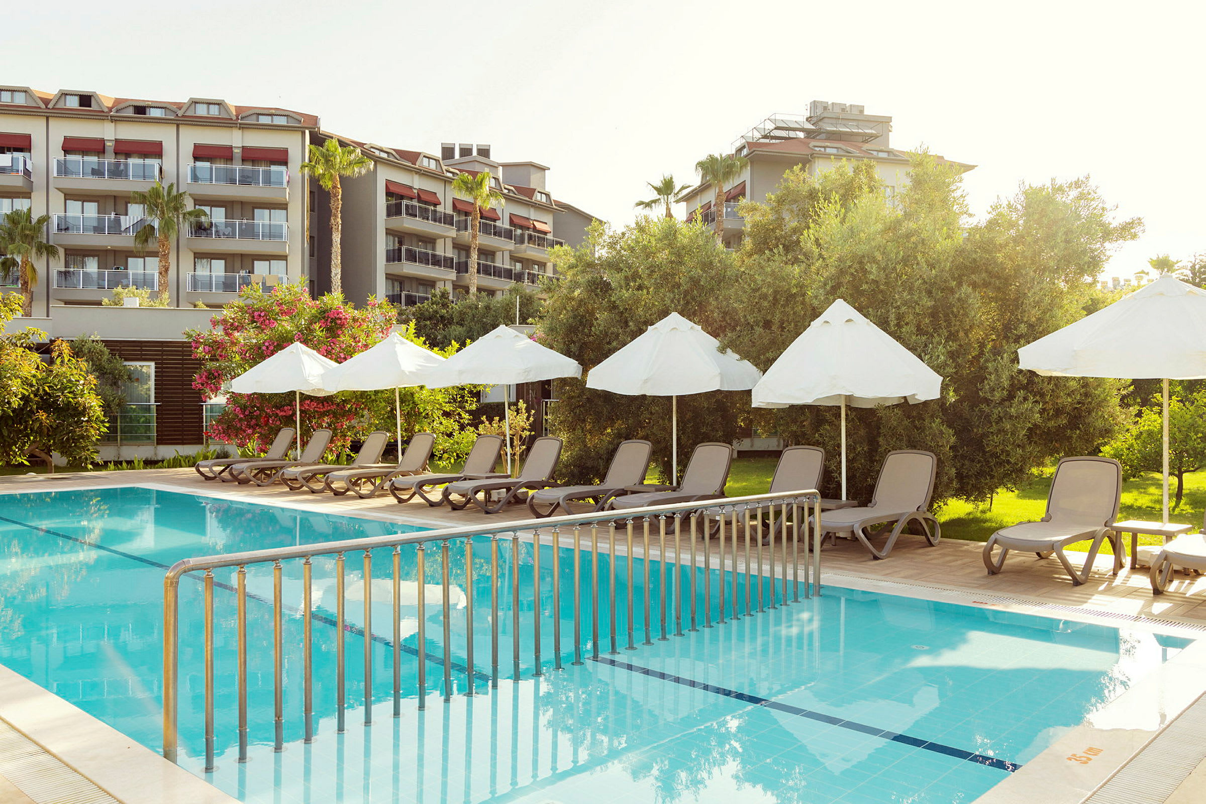 Stole og parasoller ved en pool med et hotel i baggrunden. (AI-genereret tekst)