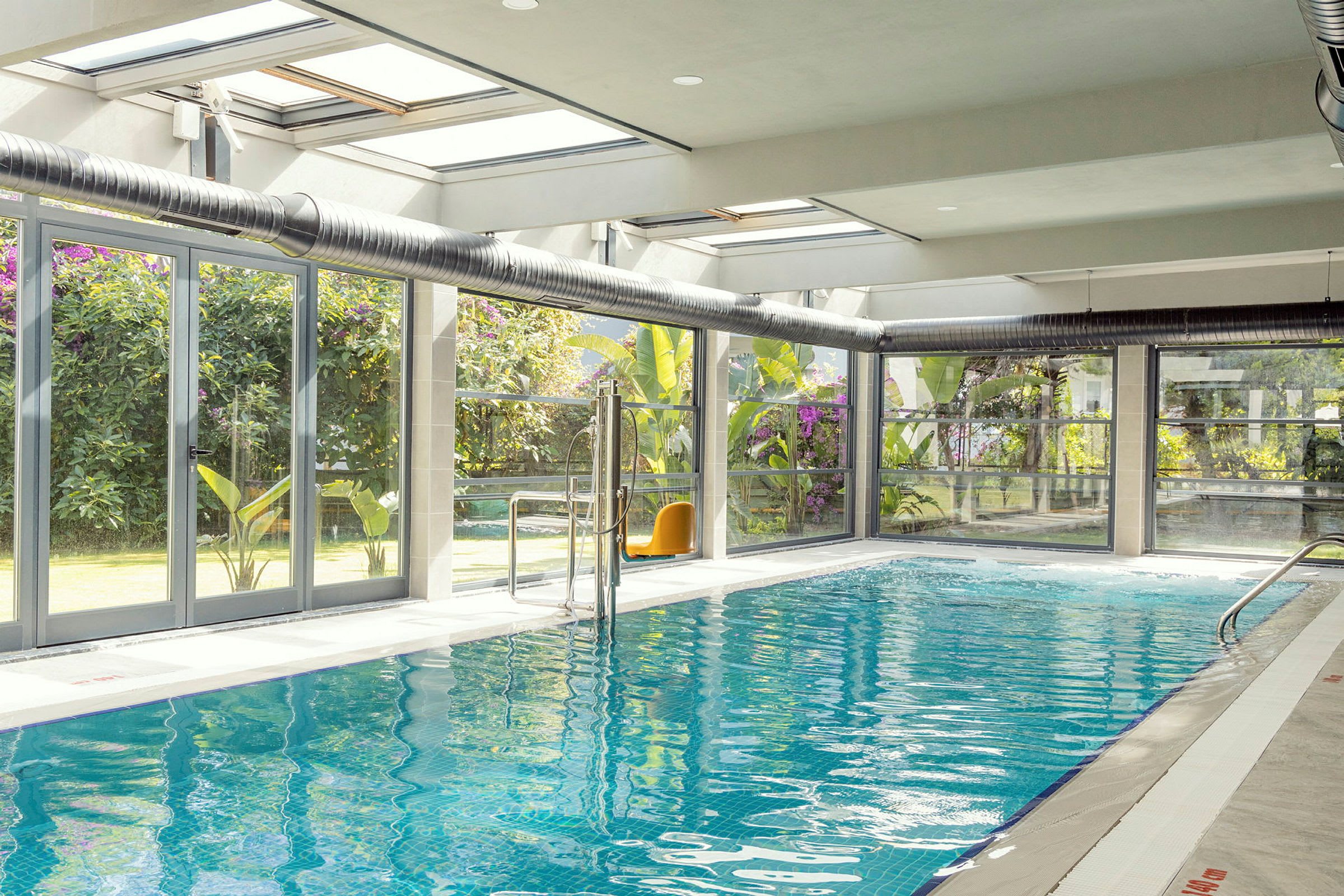 Indendørs swimmingpool med glasvægge og udsigt til haven. (AI-genereret tekst)