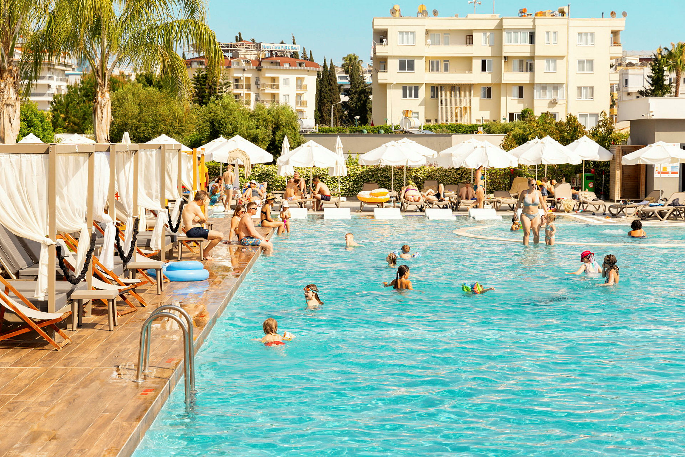 Folk nyder en pool omgivet af solsenge og parasoller på et hotelområde. (AI-genereret tekst)