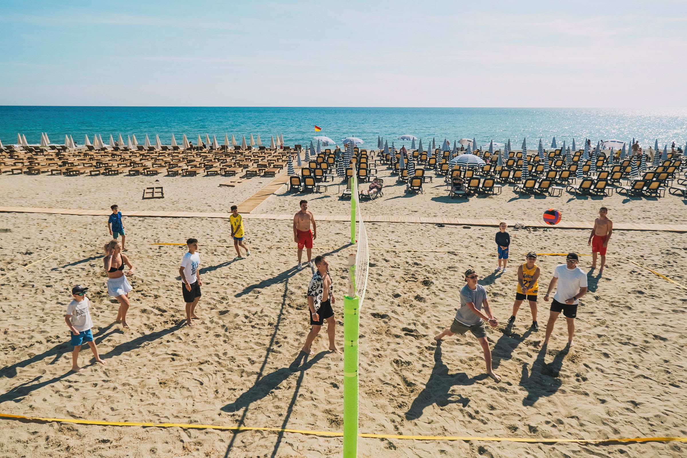 En strand med liggestole og parasoller, folk spiller volleyball. (AI-genereret tekst)