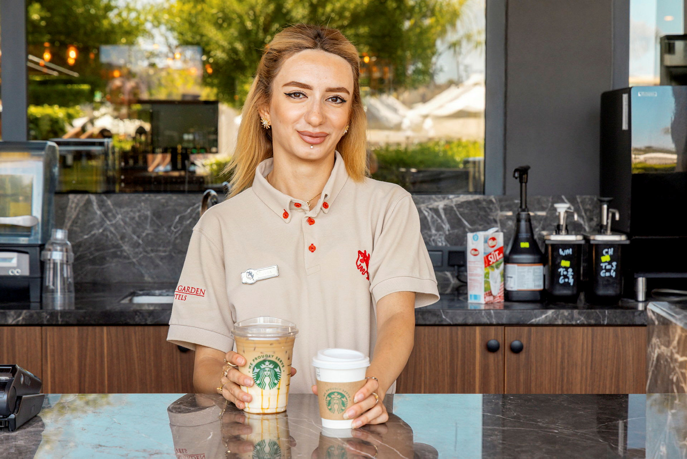 En kvinde står bag en disk og holder to kaffekopper fra Starbucks. (AI-genereret tekst)
