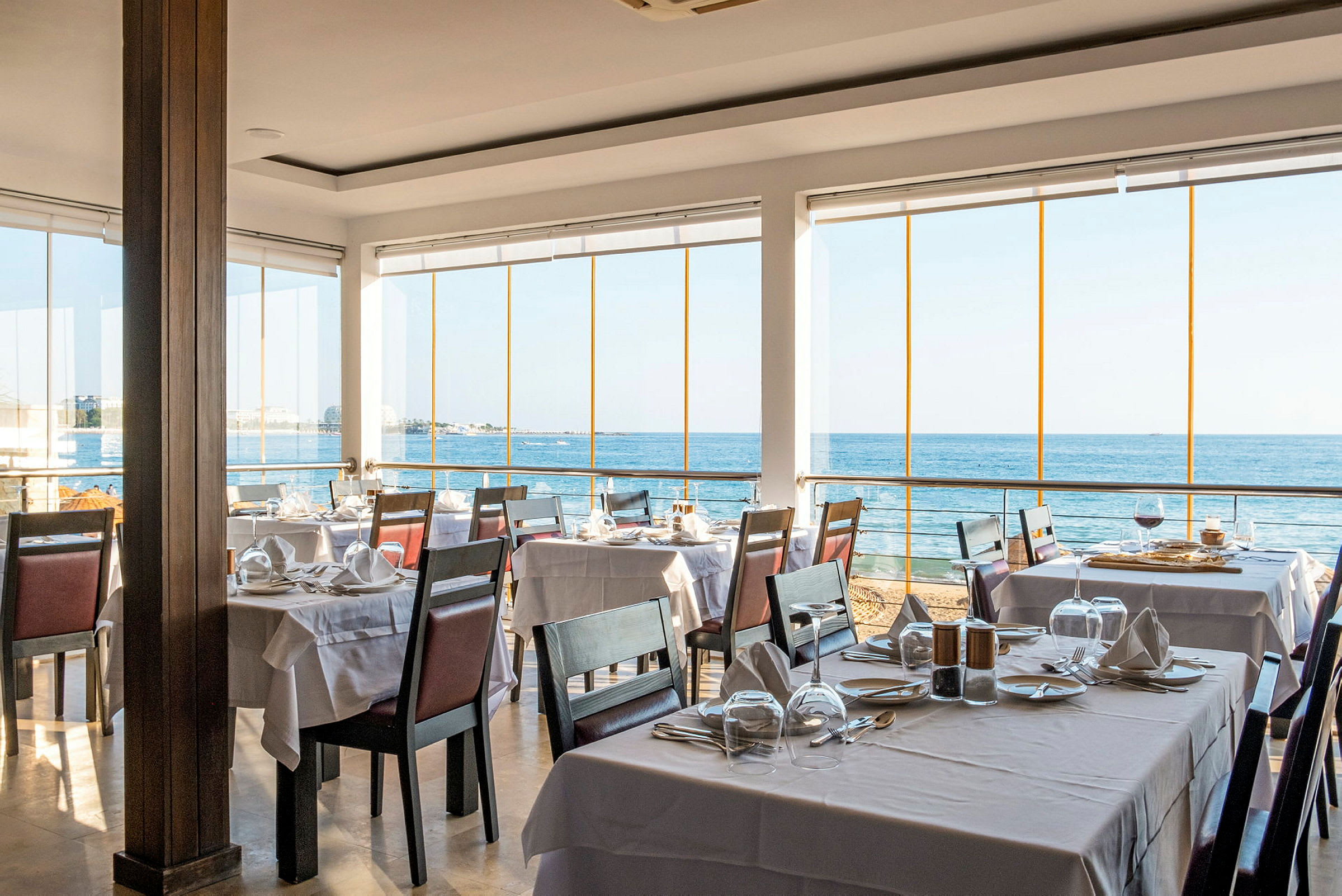 Restaurant med dækkede borde og udsigt over havet. (AI-genereret tekst)