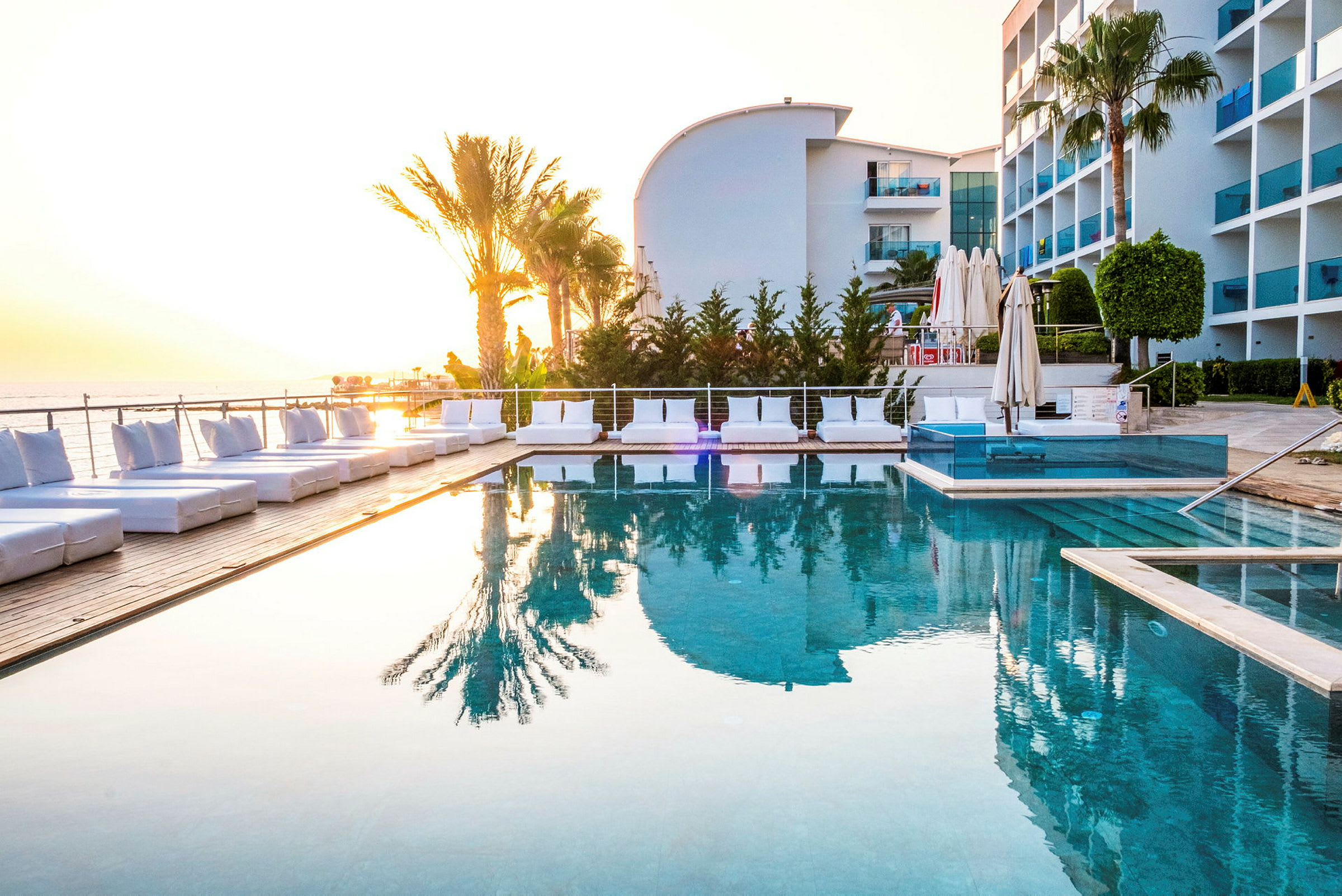 Udendørs swimmingpool omgivet af solsenge og palmer, med hotelbygning i baggrunden. (AI-genereret tekst)
