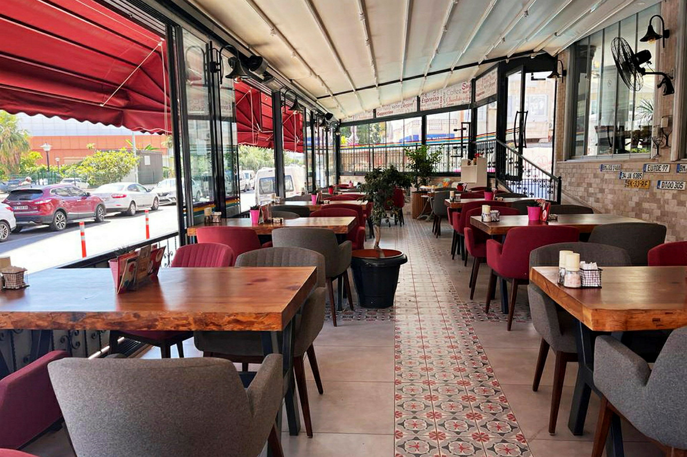 Billede af en restaurant med rødt interiør, træborde og bløde stole. Udsigt over gaden ses gennem glasvinduer. (AI-genereret tekst)