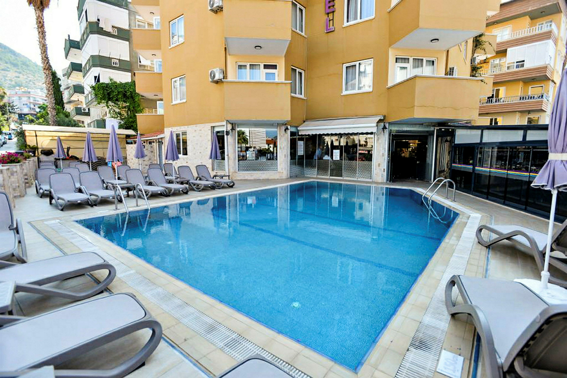 En udendørs swimmingpool omgivet af liggestole og parasoller ved en bygning. (AI-genereret tekst)