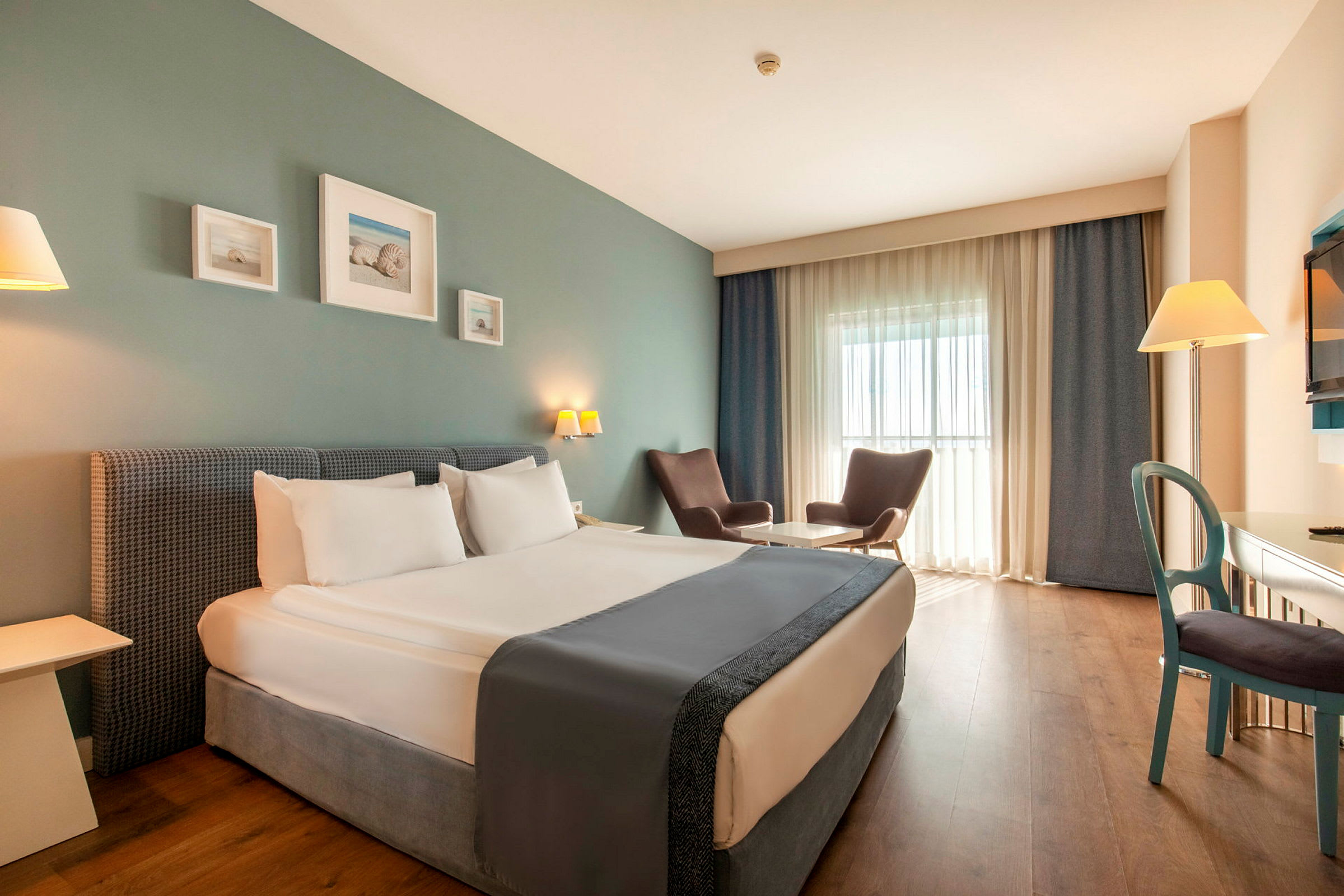 Et hotelværelse med en dobbeltseng, to lænestole ved et bord, et skrivebord og et fjernsyn. (AI-genereret tekst)
