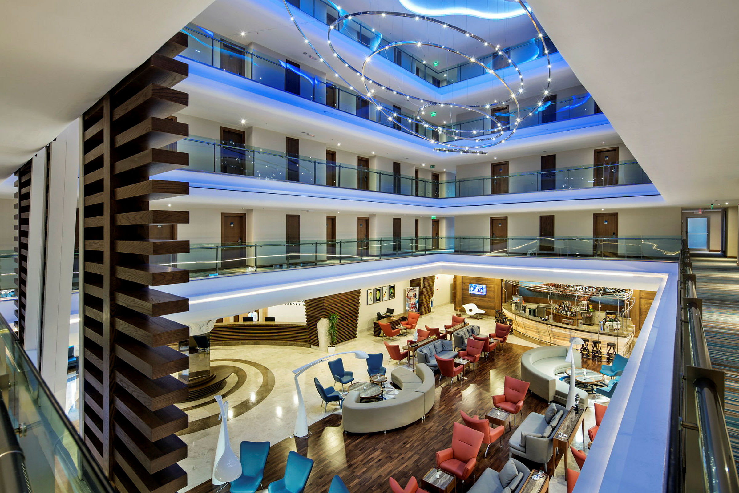 Et interiørbillede af et hotel med flere etager, glasgelændere, siddegrupper og en reception. (AI-genereret tekst)