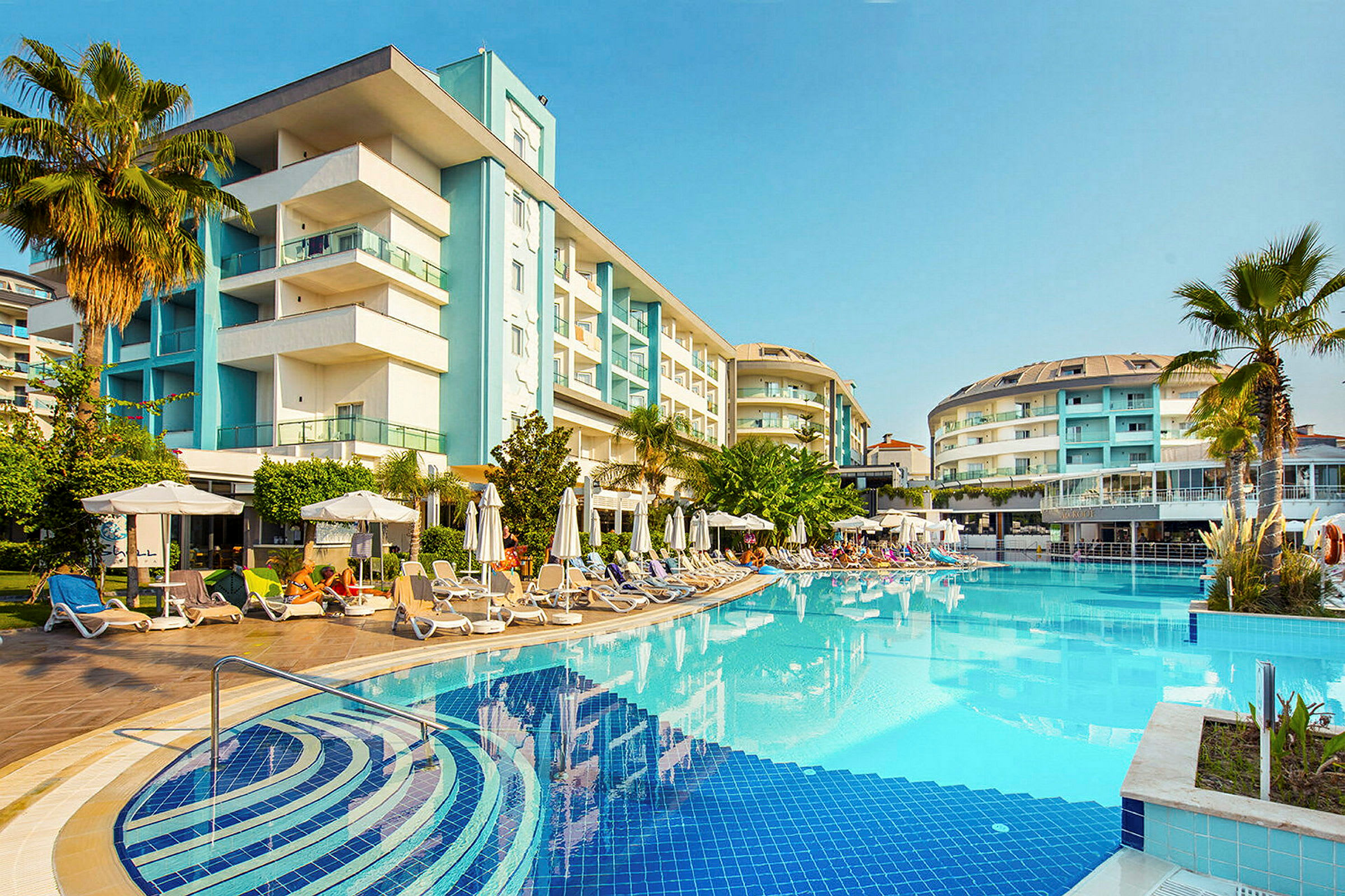 Hotel bygget omkring en udendørs pool med liggestole og parasoller. (AI-genereret tekst)