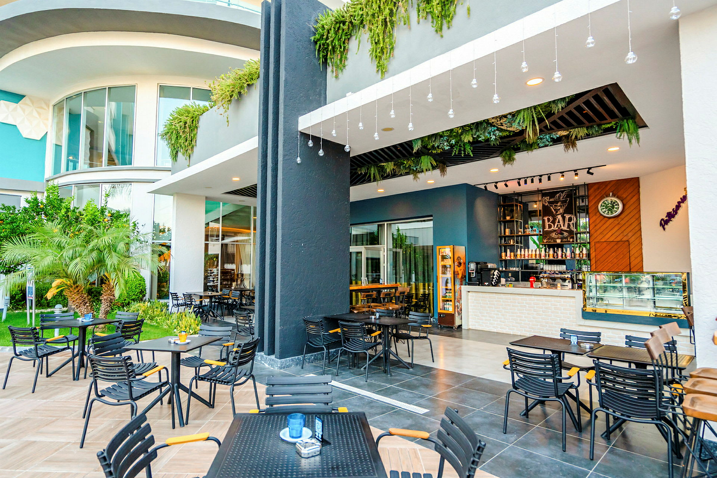 Udendørsmiljø med borde og stole foran en moderne bar med planteudsmykning og glasfacade. (AI-genereret tekst)