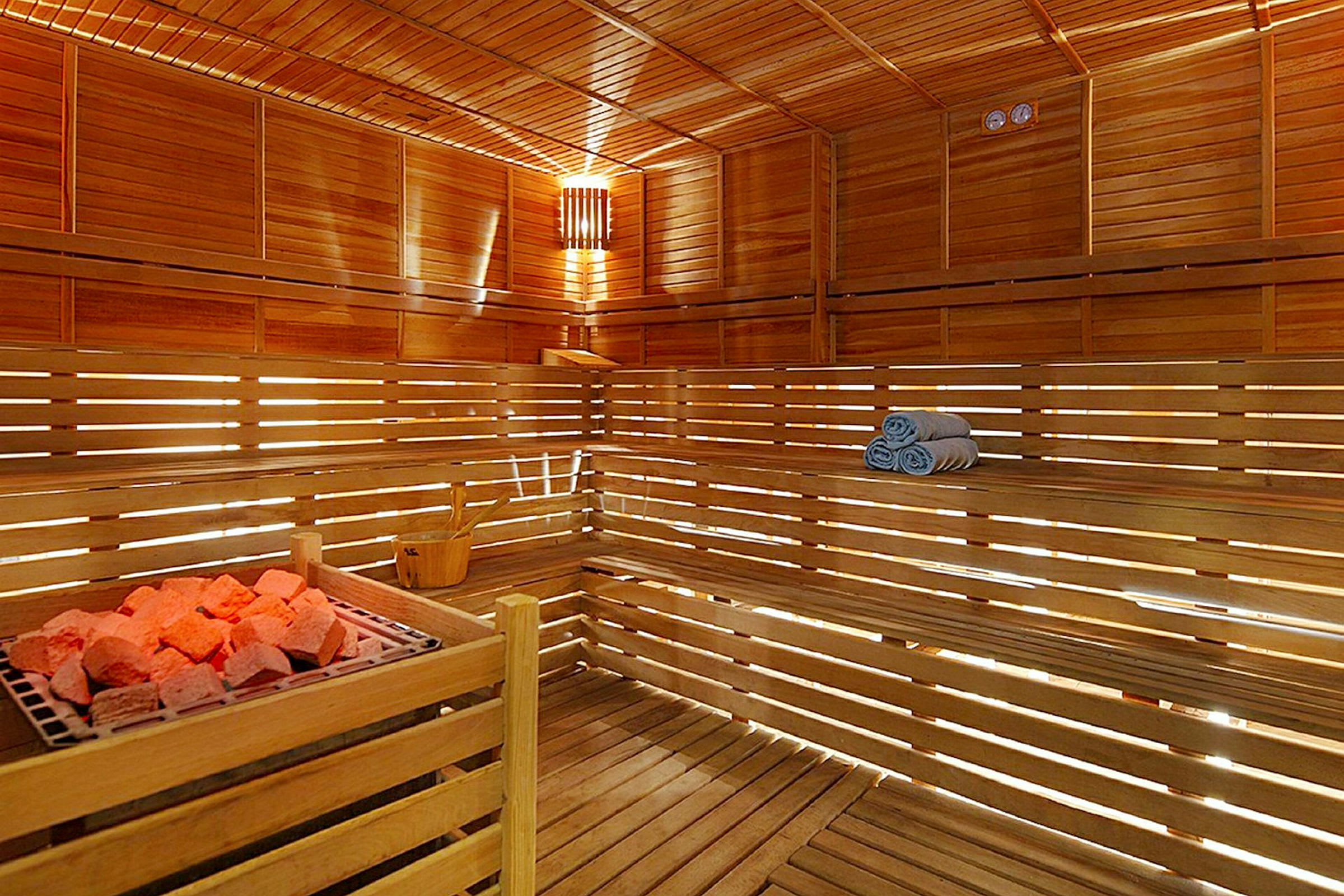 Inderummet af en sauna med træpaneler, træbænke, rød-belysede saunasten og sammenrullede håndklæder. (AI-genereret tekst)
