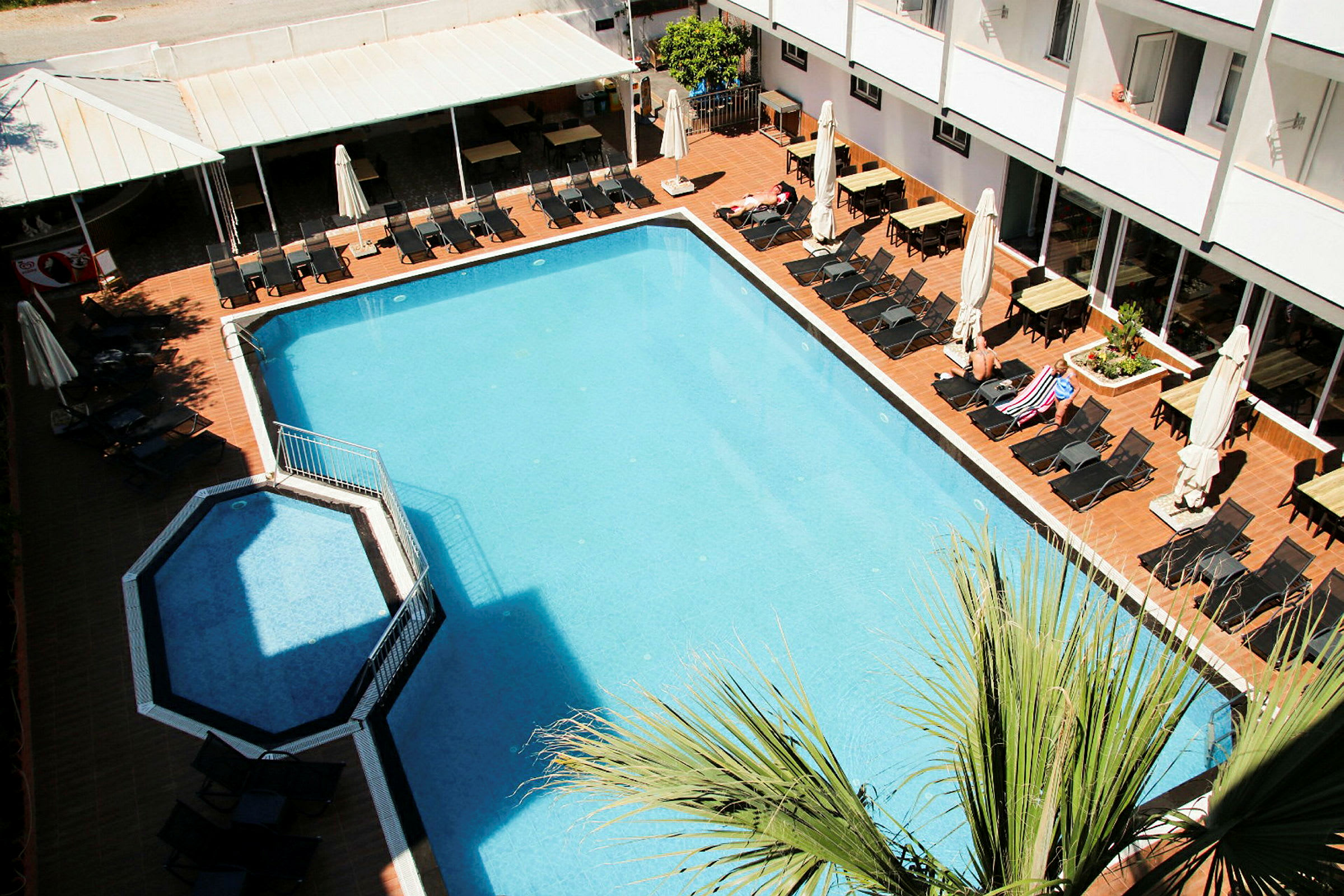 En rektangulær swimmingpool med liggestole og parasoller omkring på en terrasse. (AI-genereret tekst)