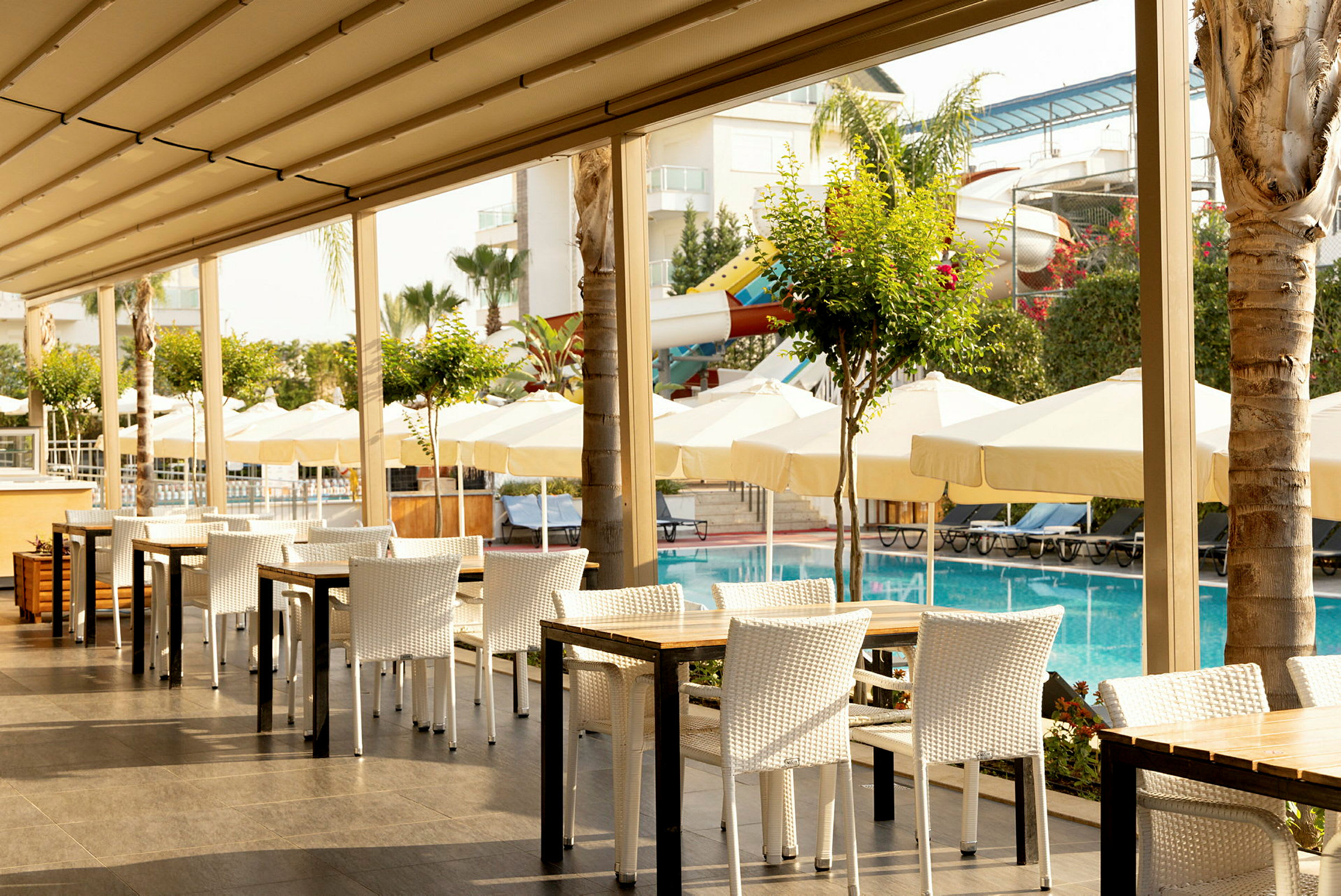 Udendørs restaurant ved en pool med parasoller og liggestole i baggrunden. (AI-genereret tekst)