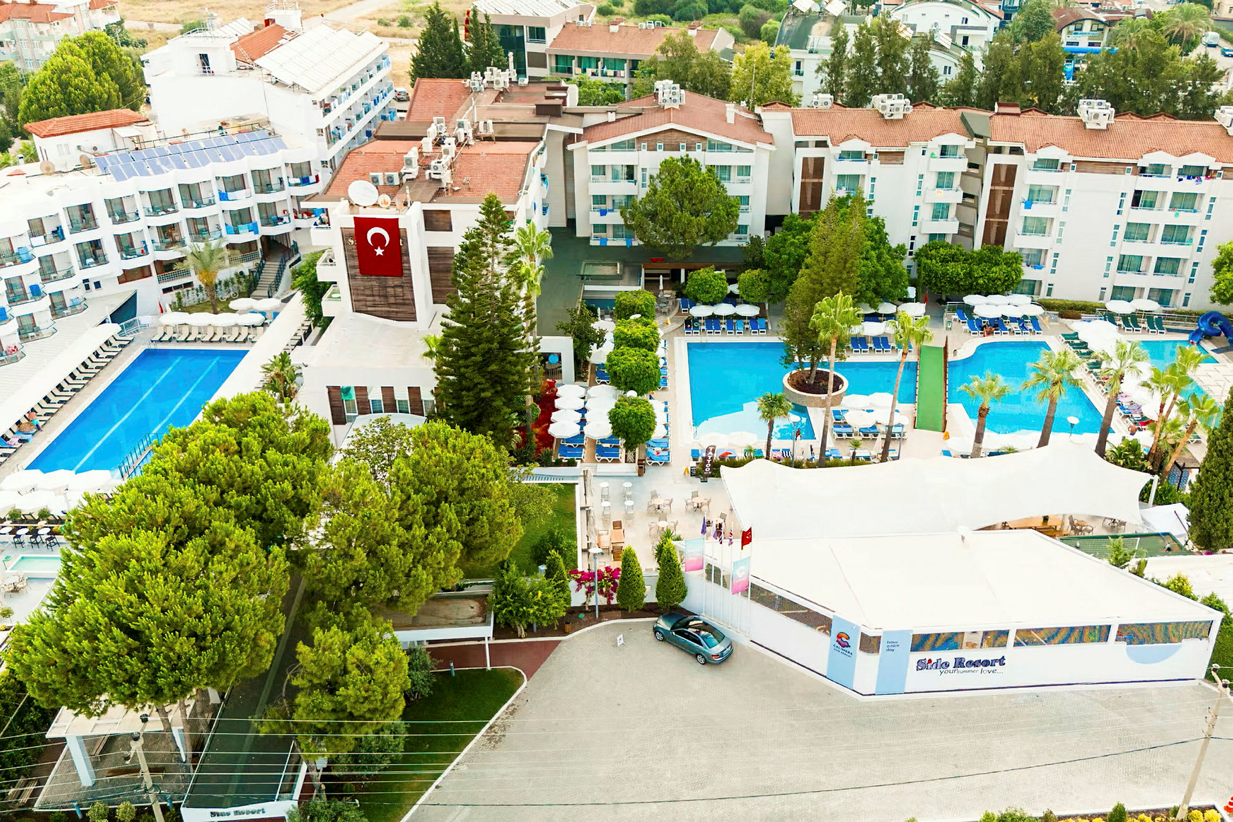 Et luftfoto af et hotelområde med pools, bygninger og grønne træer. (AI-genereret tekst)