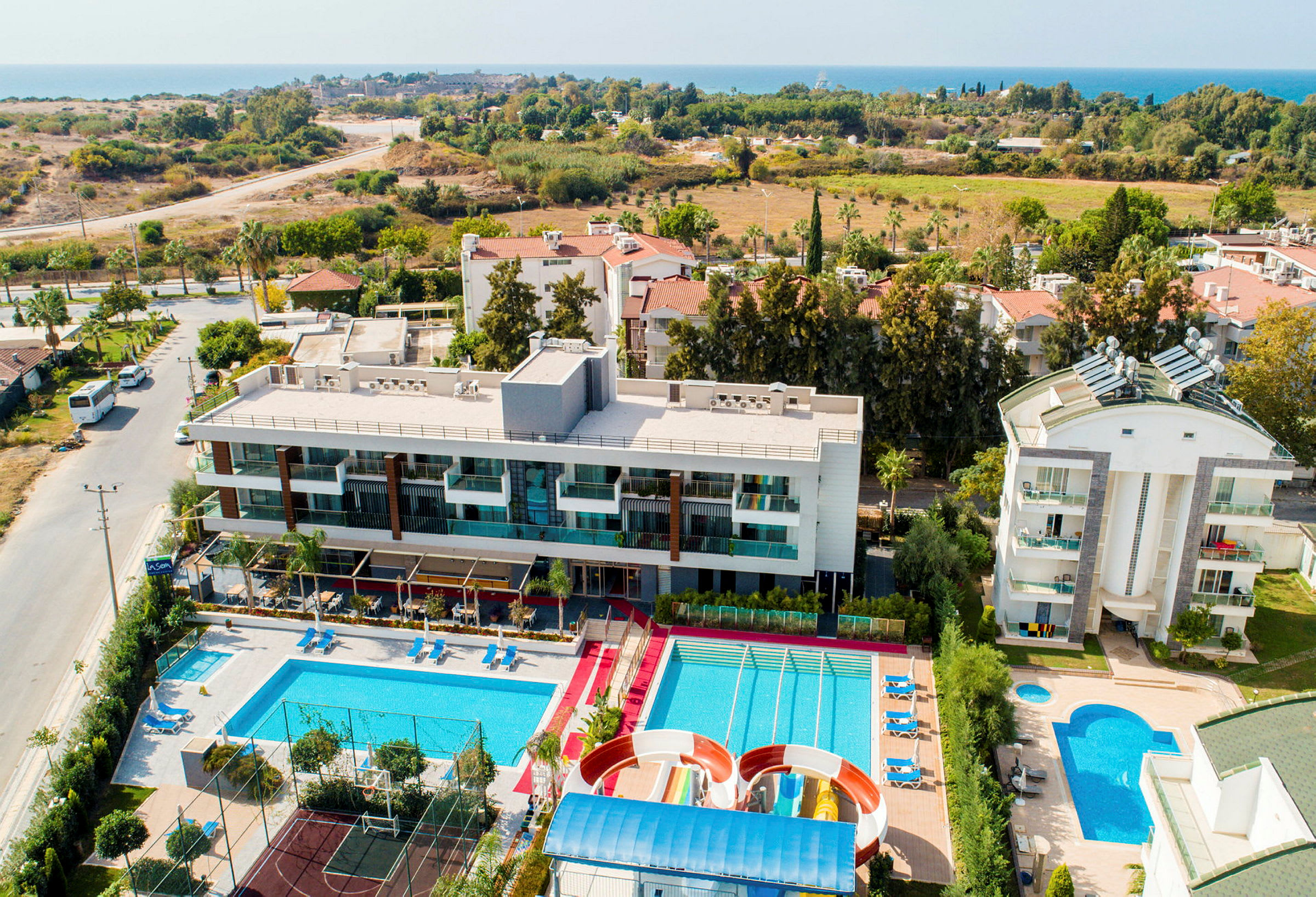 Et hotelkompleks med swimmingpools, vandrutsjebaner og en sportsbane. Havet og landskabet i baggrunden. (AI-genereret tekst)