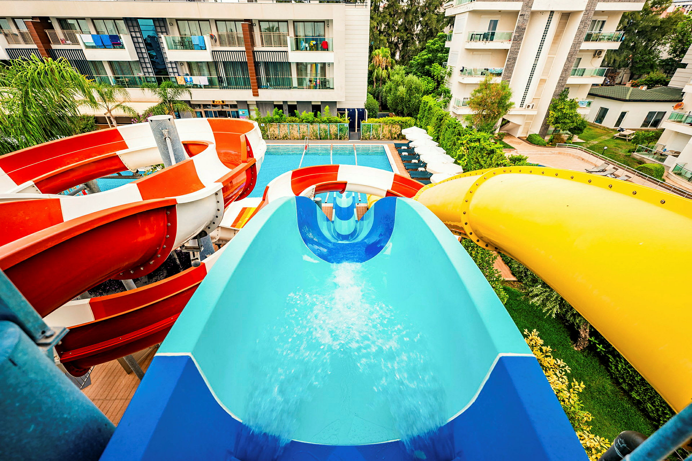 Vandrutsjebaner i forskellige farver fører til en pool på et hotelområde. (AI-genereret tekst)