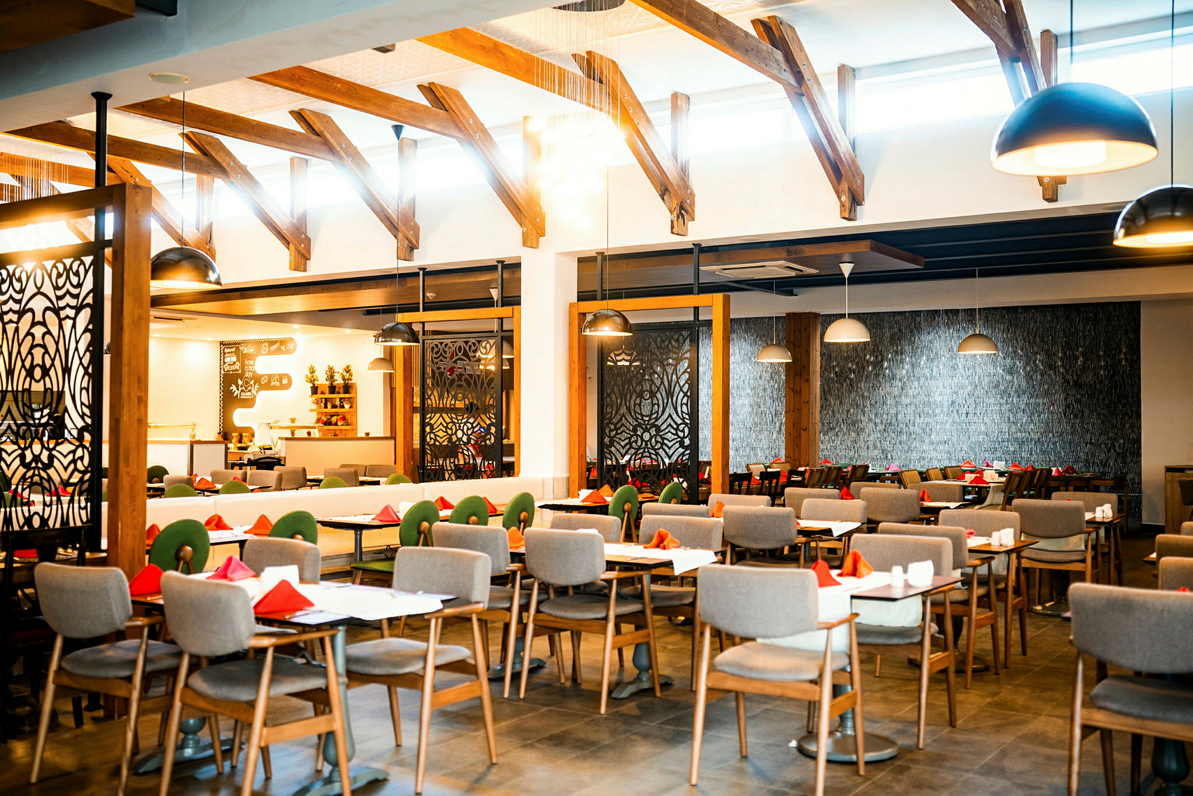 Interiøret i en restaurant med opstillinger af dækkede borde og stole, med loftsbjælker og moderne designede lamper. (AI-genereret tekst)