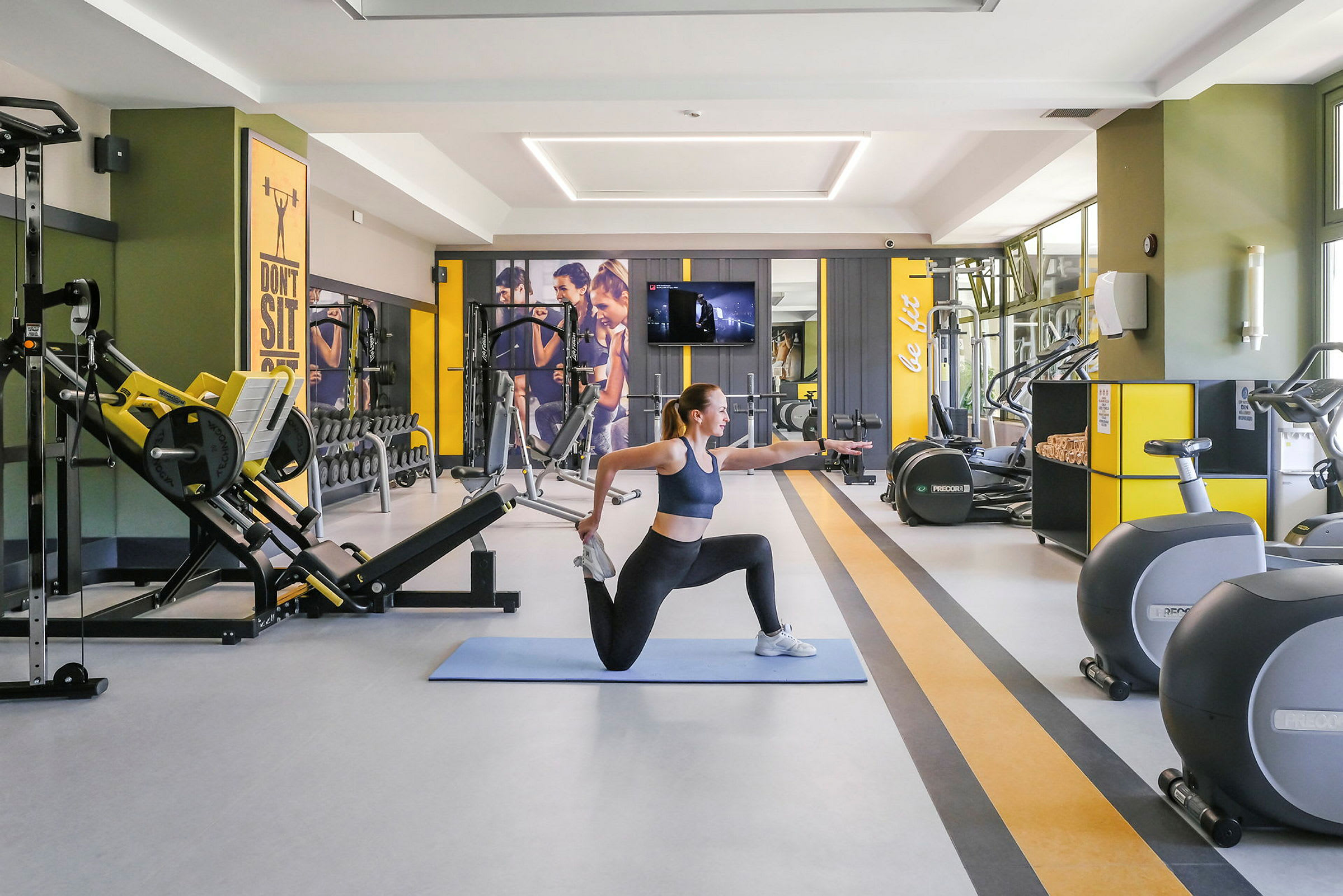 En kvinde laver strækøvelser på en træningsmåtte i et fitnesscenter. (AI-genereret tekst)