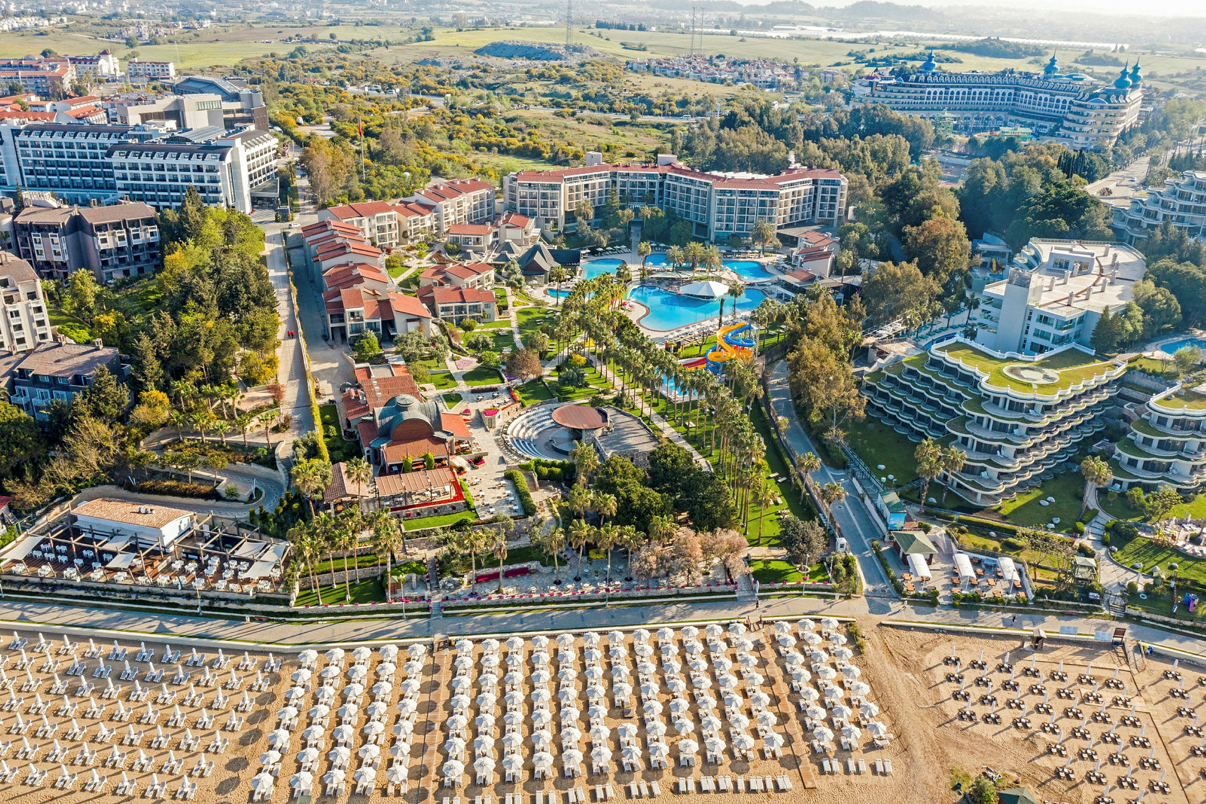Hotelkompleks med pool, haver og strand med liggestole og parasoller. (AI-genereret tekst)
