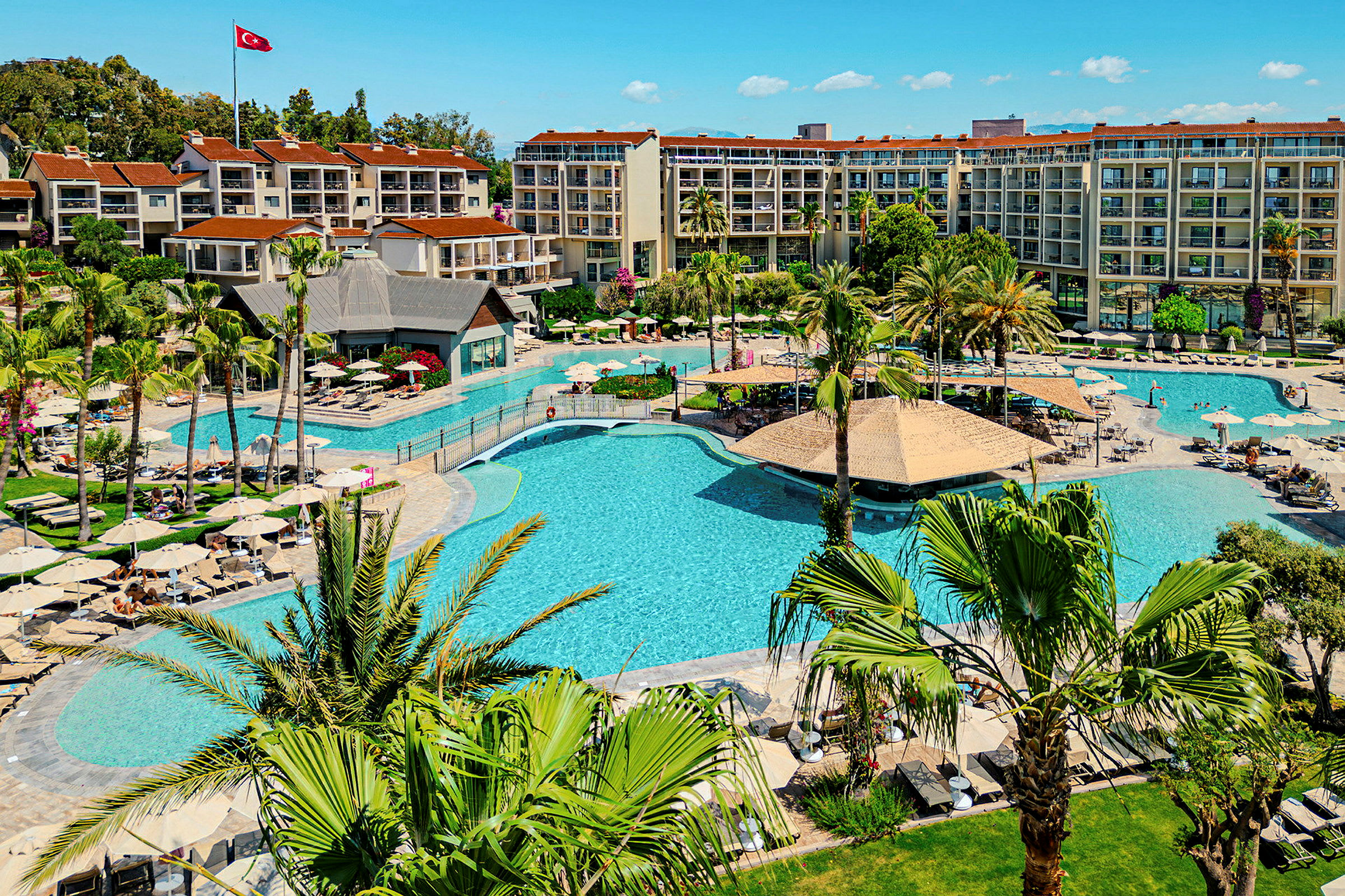 Hotel med store udendørs swimmingpools og omkringliggende grønne områder. (AI-genereret tekst)