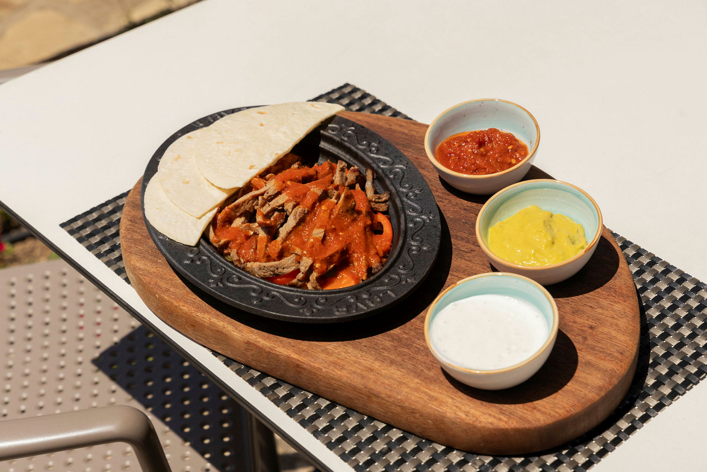 En tallerken med kød, grøntsager og saucer samt tortillabrød på en træbakke. (AI-genereret tekst)