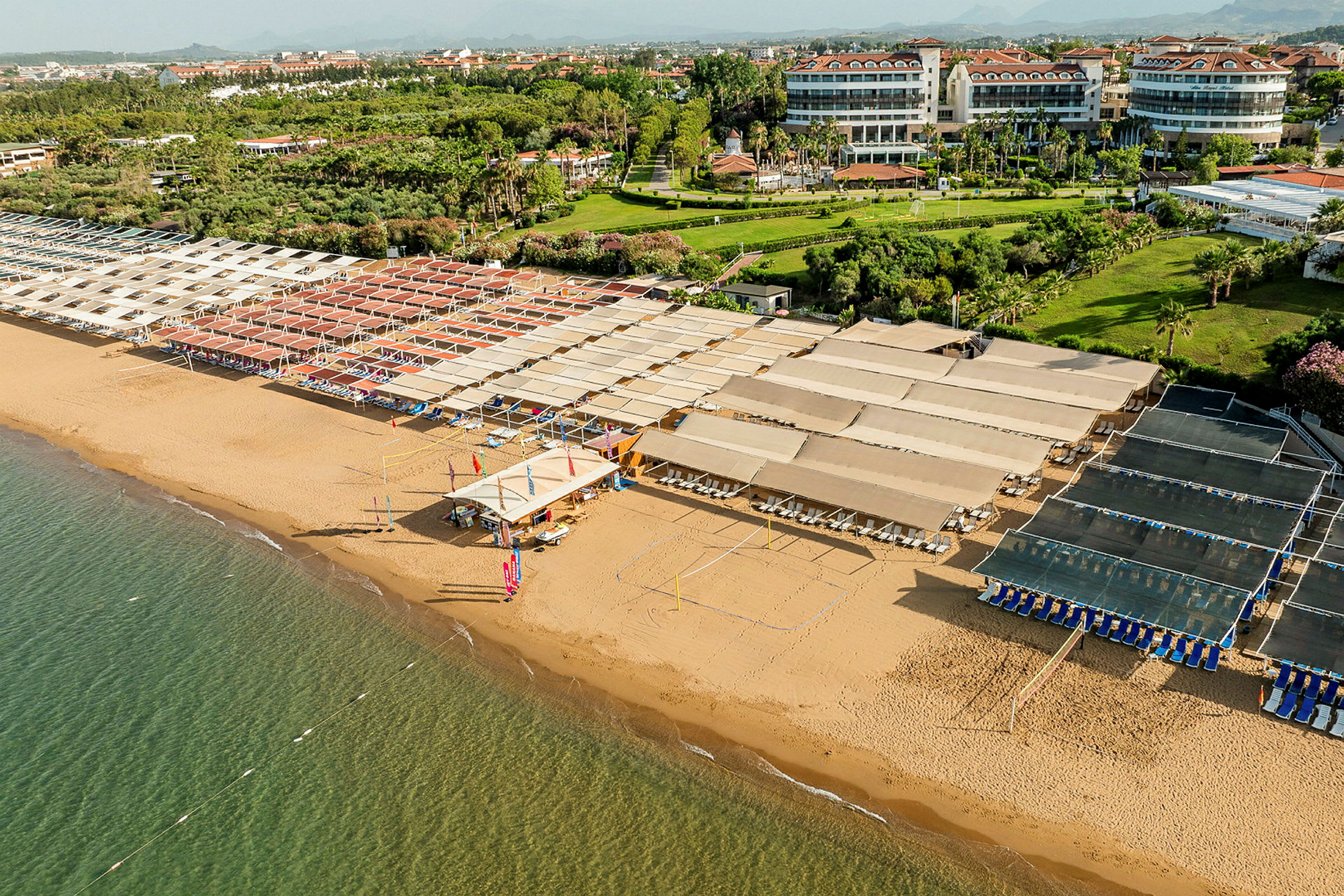 Strand med solafskærmning, liggestole og grønne områder i baggrunden. (AI-genereret tekst)