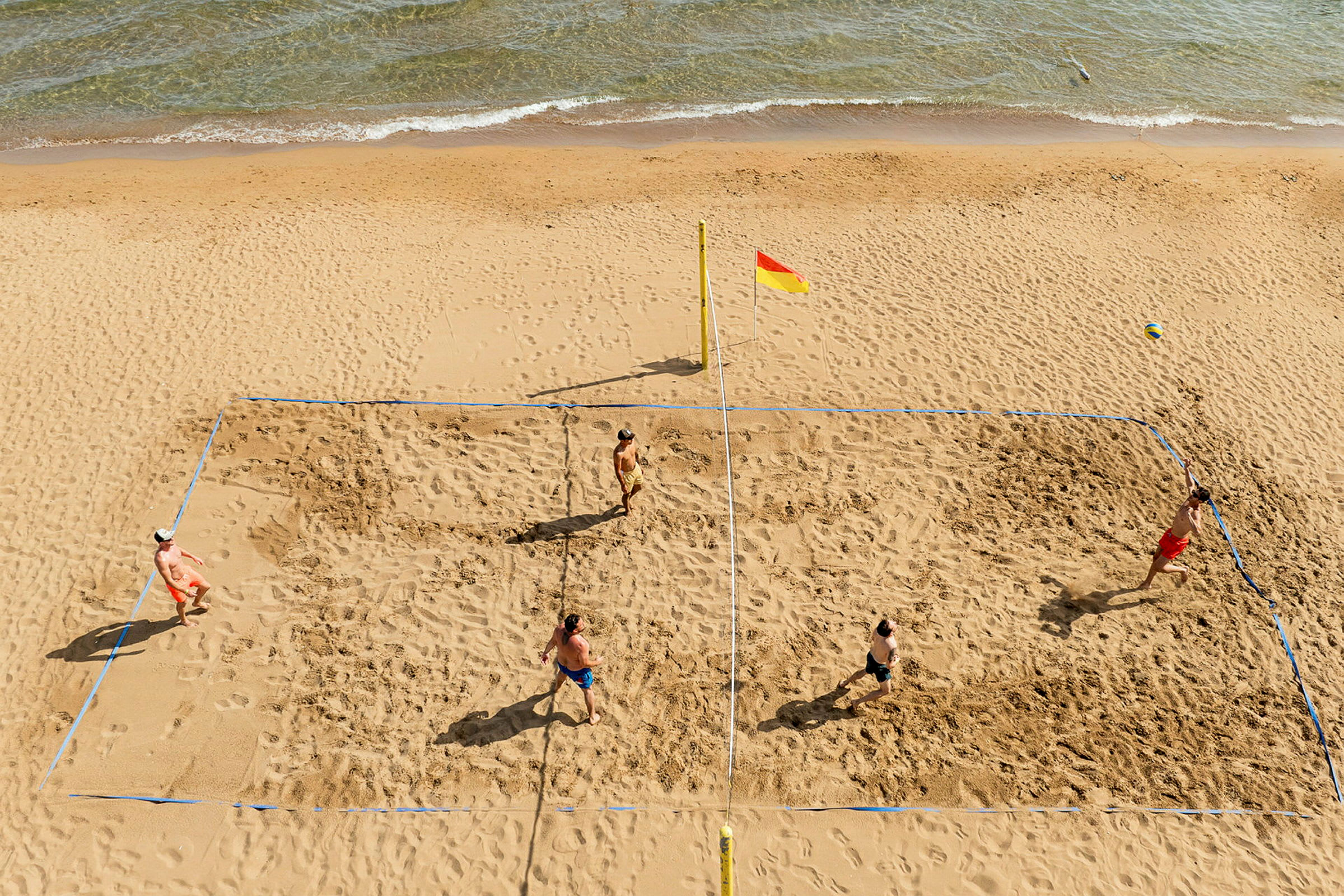 Fire personer spiller strandvolleyball på en sandstrand tæt på havet. (AI-genereret tekst)