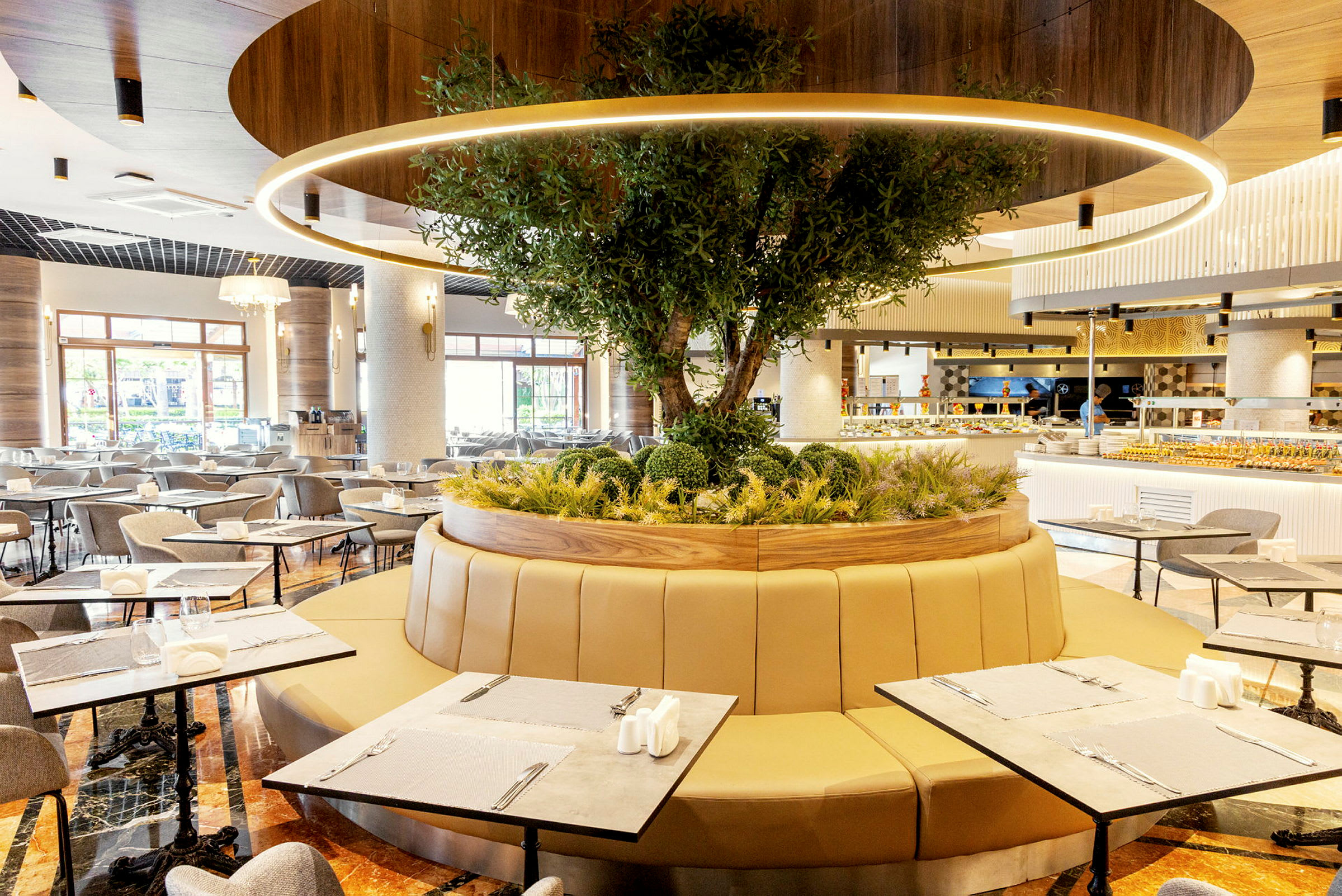 Et moderne restaurantområde med siddepladser omkring et cirkulært planteområde med et træ. (AI-genereret tekst)