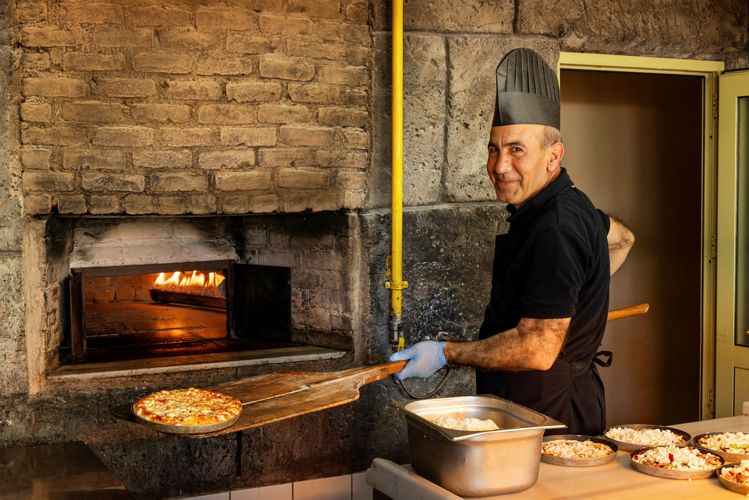 En pizzabager tager en pizza ud af en stenovn, klar til servering. (AI-genereret tekst)