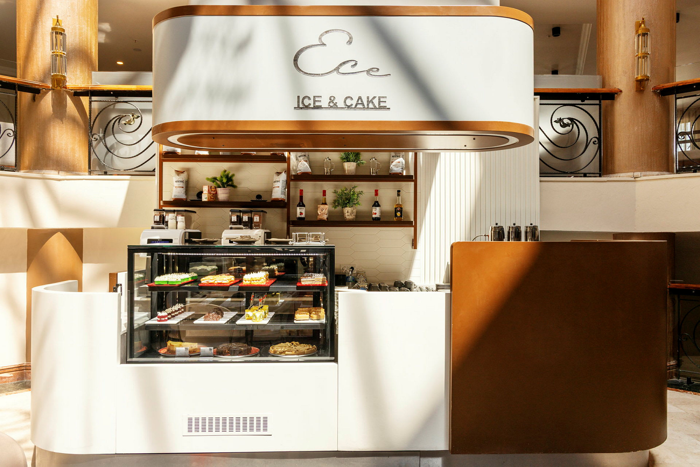 En café med glasmontrer, der viser forskellige bagværk, skilt med teksten 'Ice & Cake' og indretning i lyse toner. (AI-genereret tekst)