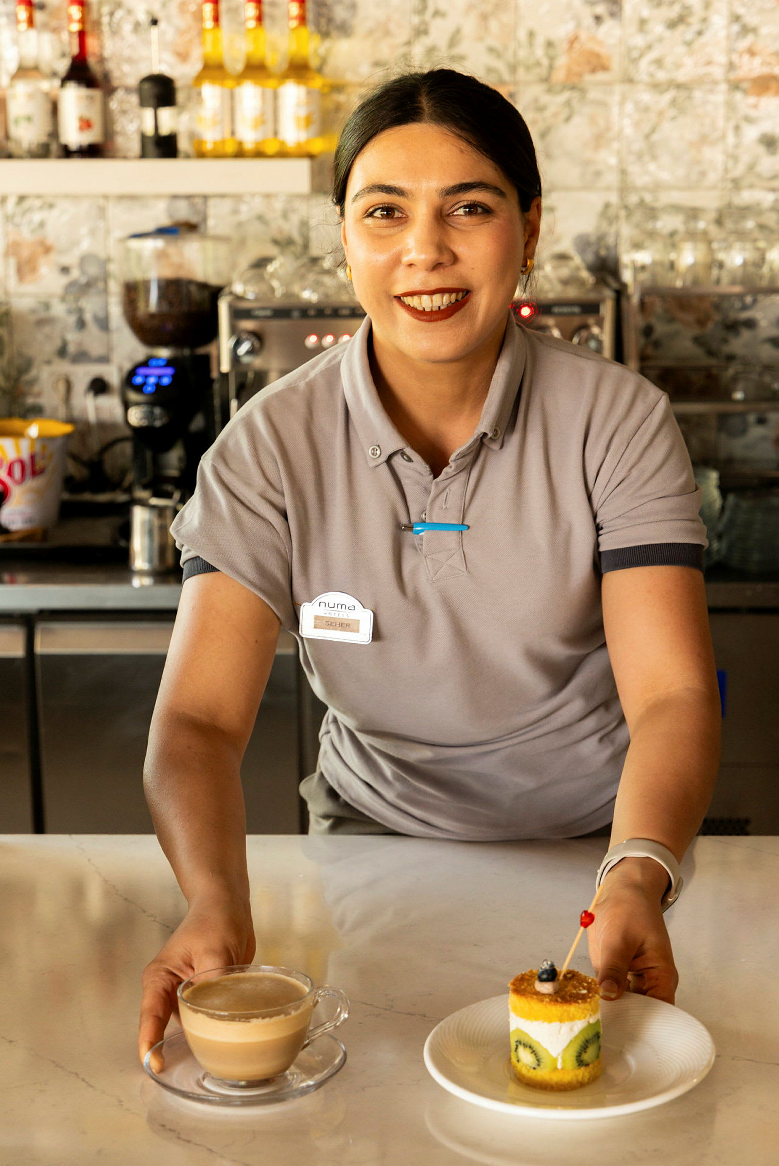 En person iført uniform holder en kop kaffe og en tallerken med en dessert kage på en disk. (AI-genereret tekst)