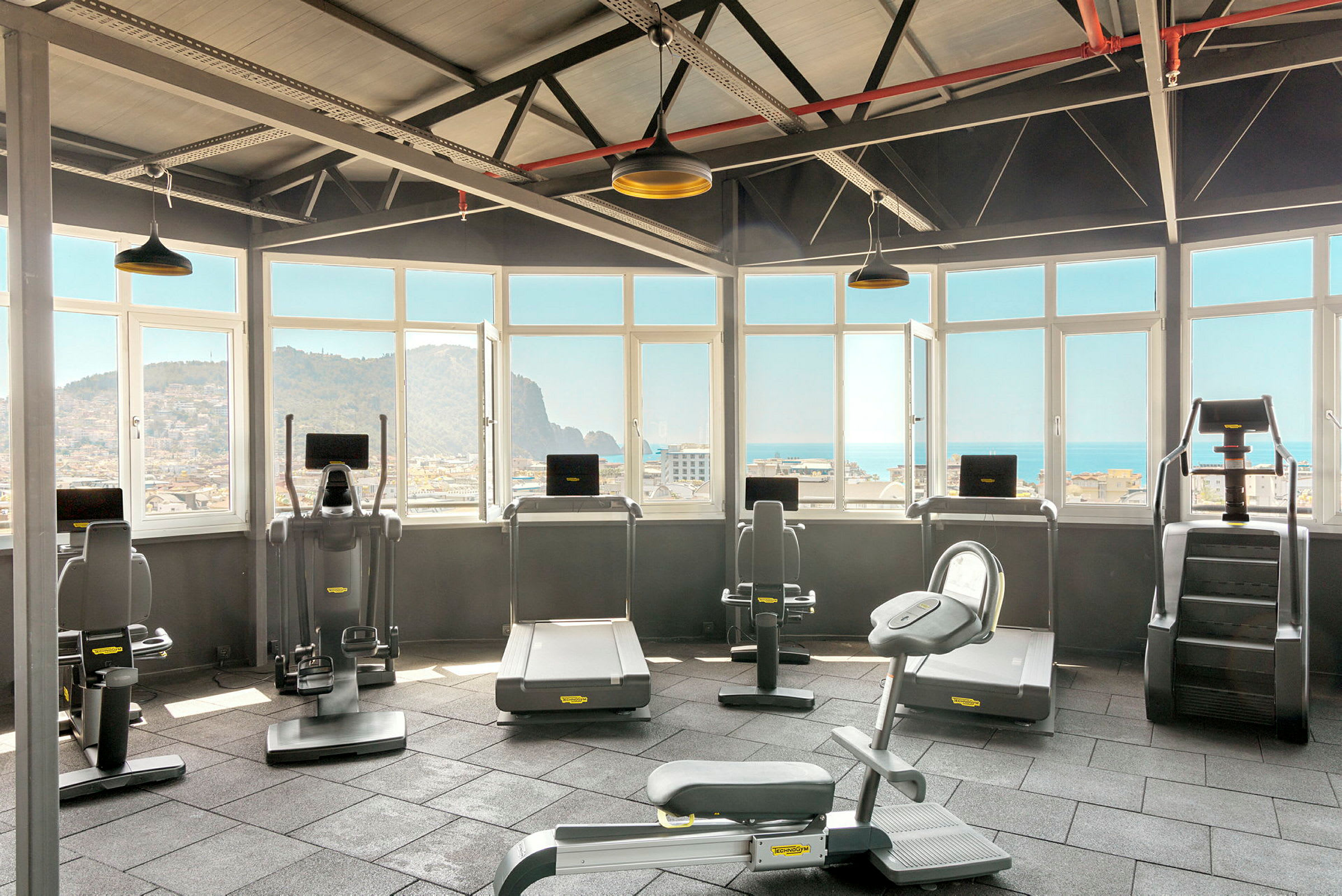 Træningsrum med fitnessmaskiner og udsigt gennem vinduer. (AI-genereret tekst)