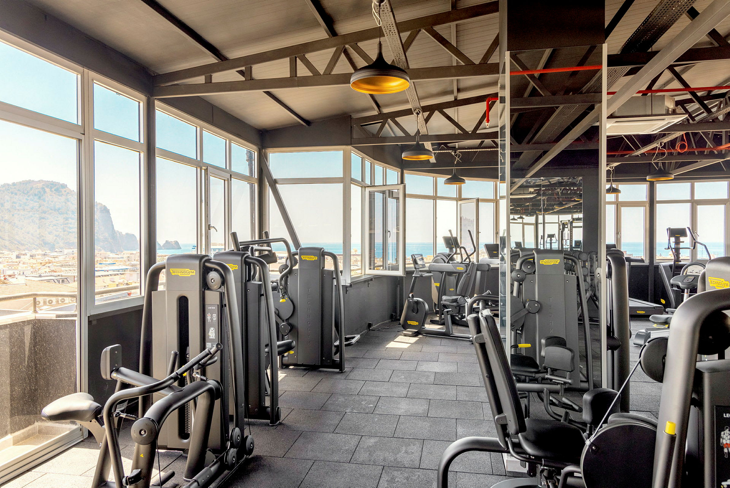 Et fitnesscenter med træningsmaskiner og store vinduer med udsigt over havet. (AI-genereret tekst)