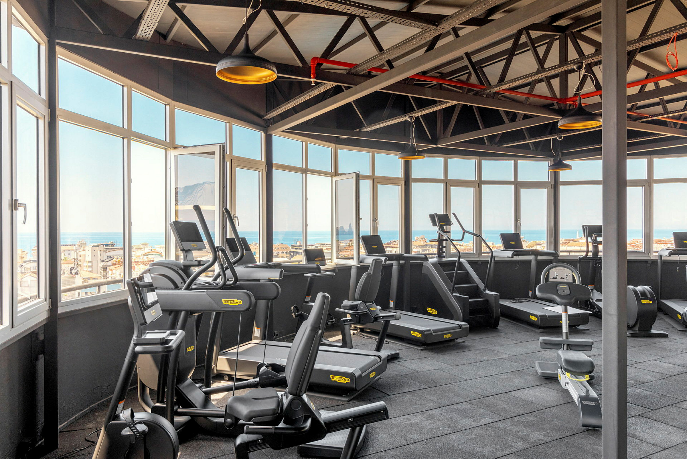 Lyst fitnesscenter med træningsmaskiner og udsigt gennem store vinduer. (AI-genereret tekst)