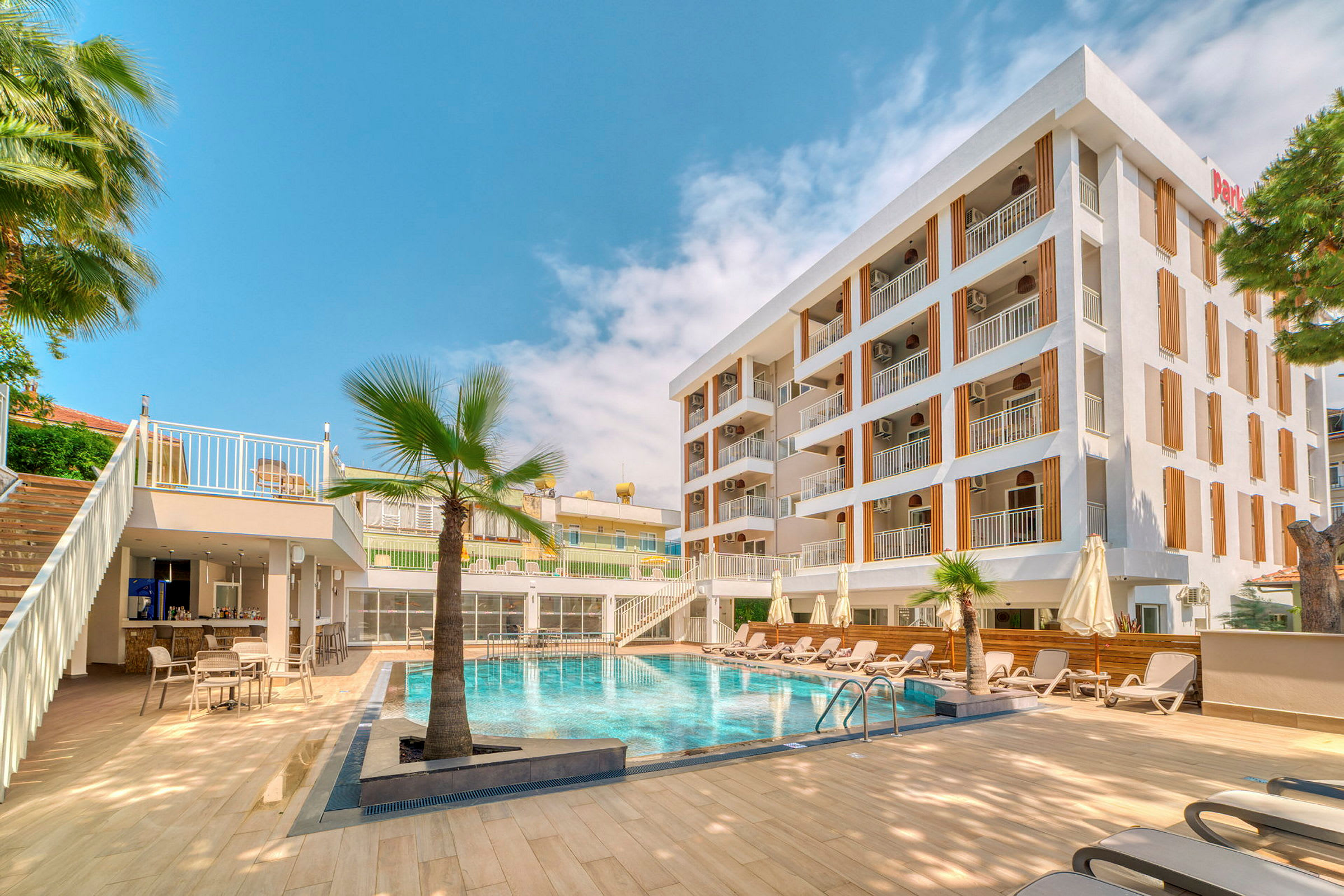 En udendørs pool med liggestole og et fleretagers hotel i baggrunden. (AI-genereret tekst)