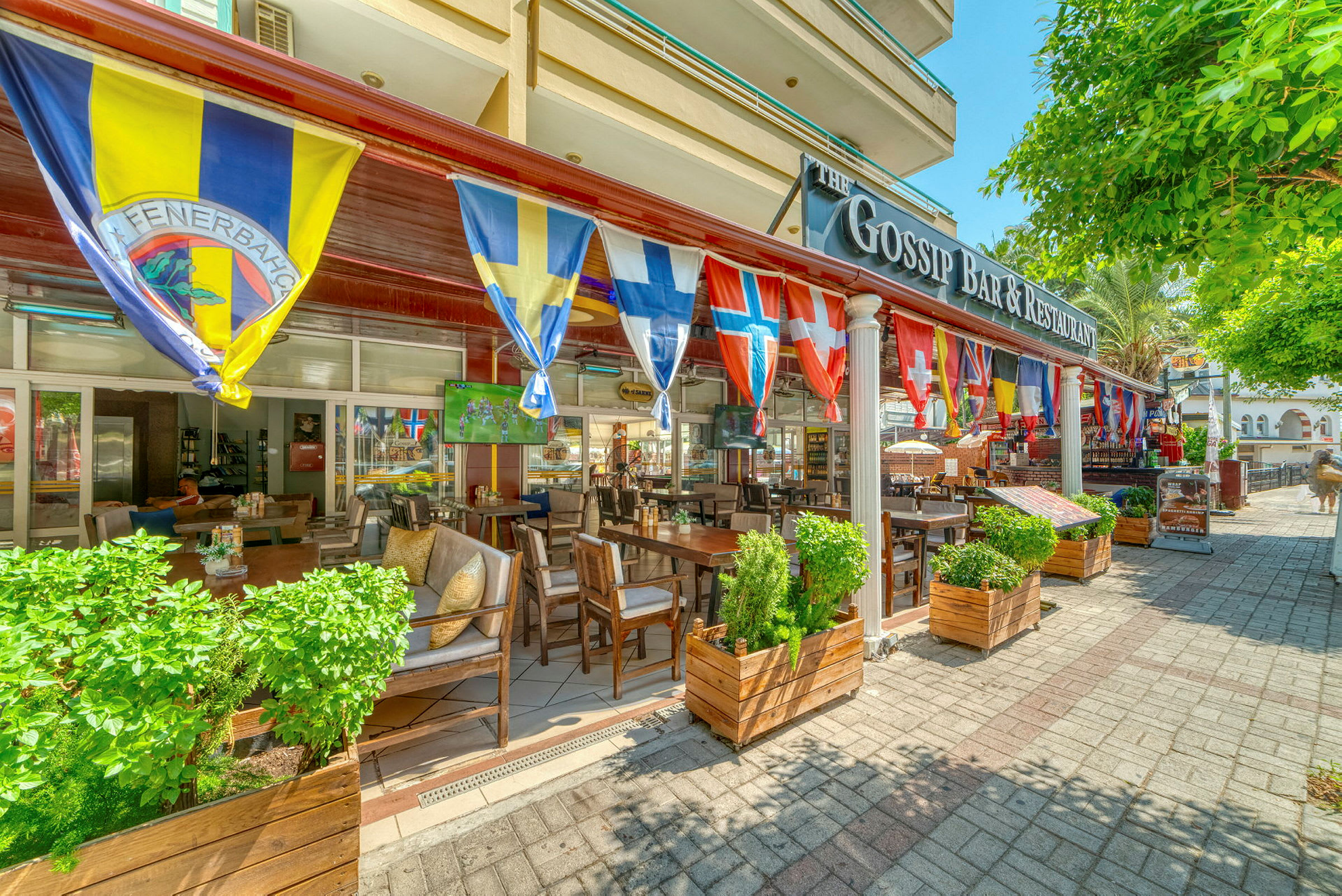 En restaurant med flag fra forskellige lande samt siddeområder udendørs. (AI-genereret tekst)
