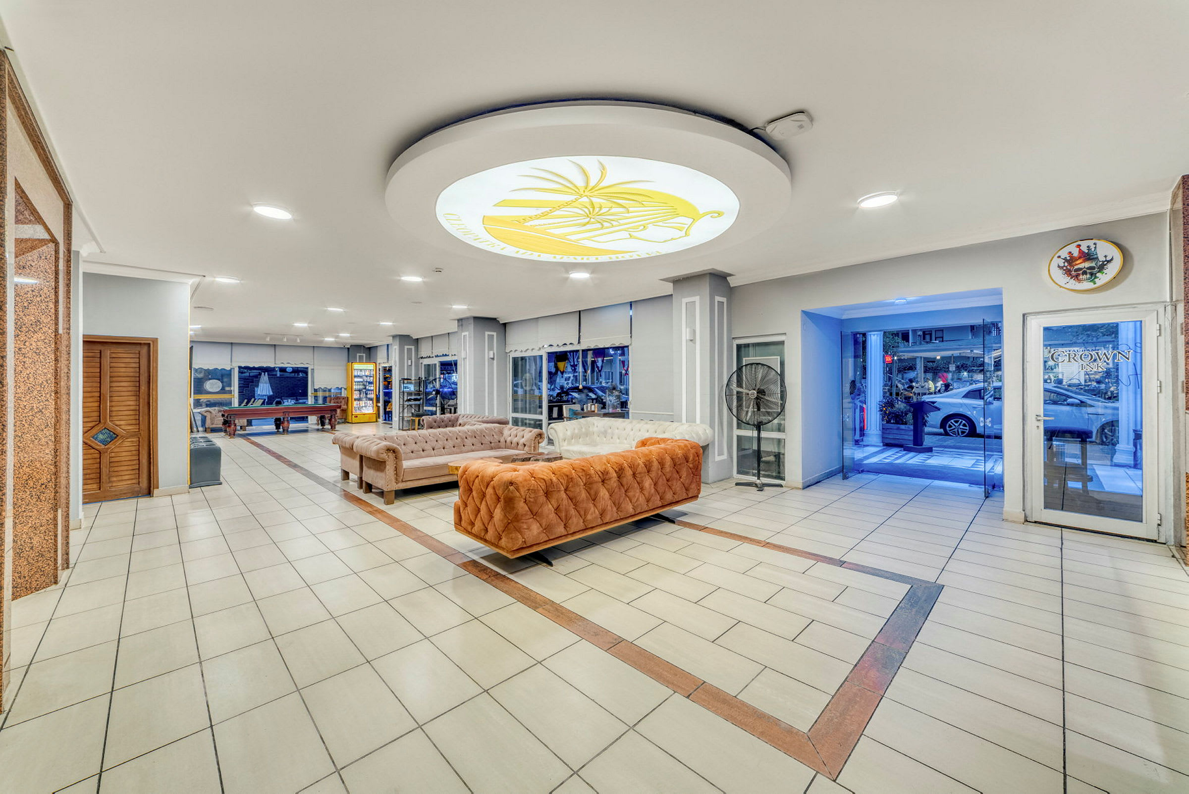 Hotellobby med sofaer, bordspil og en glasindgang. (AI-genereret tekst)