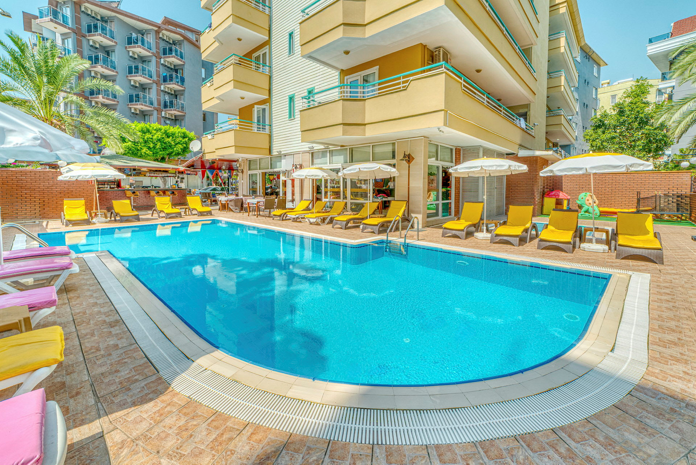 En udendørs pool omgivet af solsenge og parasoller foran en hotelbygning. (AI-genereret tekst)