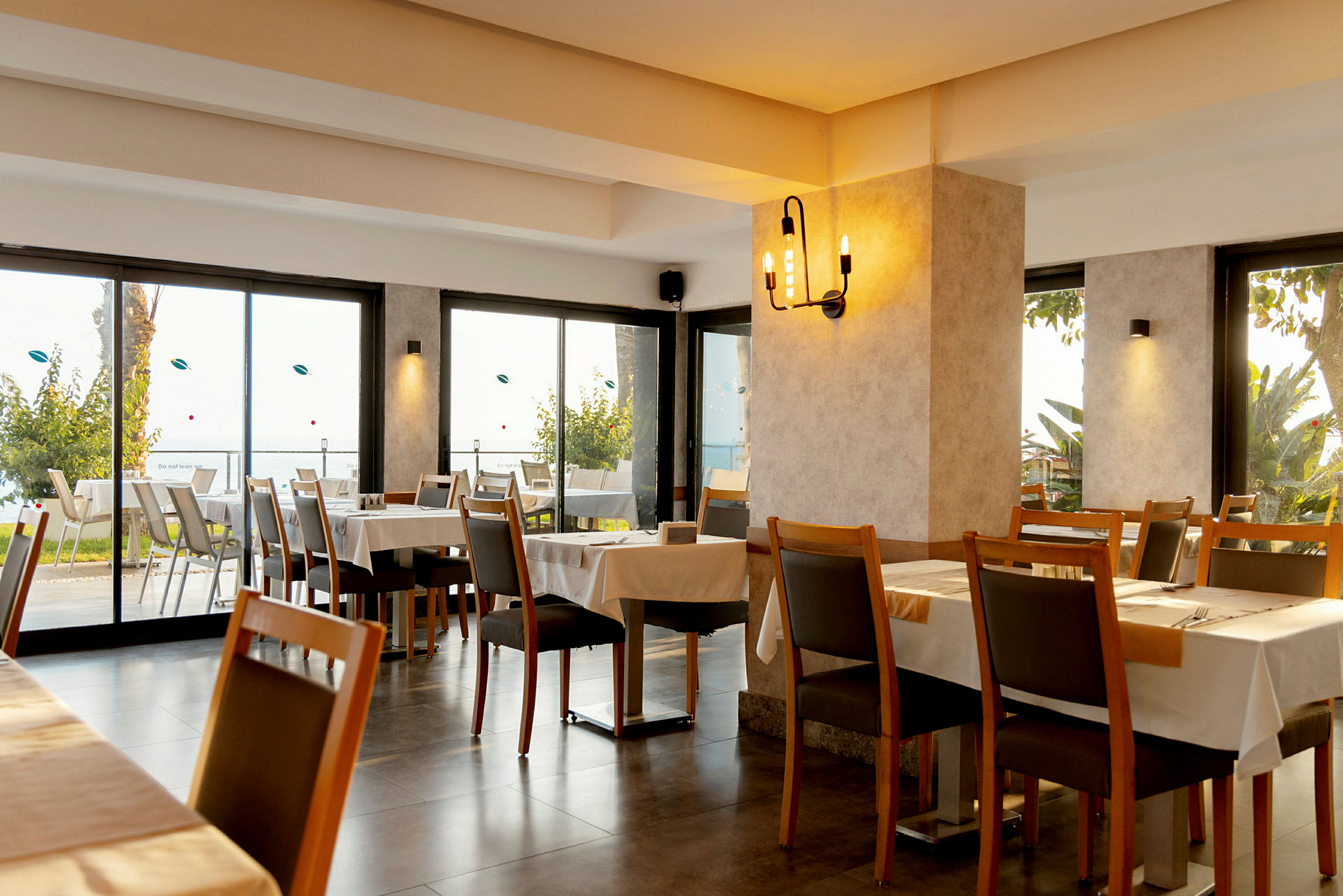 Restaurantinteriør med borde og stole samt udsyn til natur og lysindfald. (AI-genereret tekst)