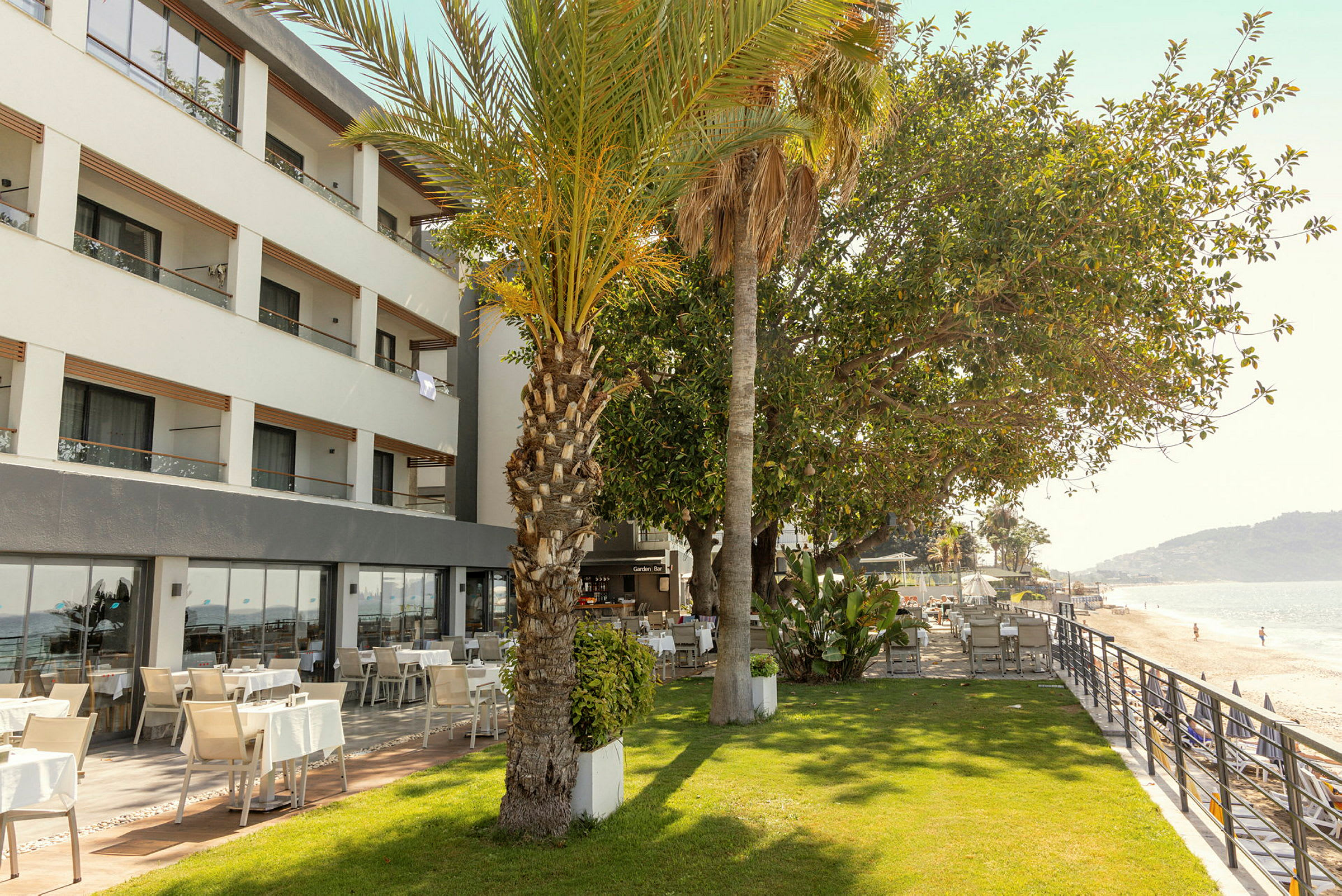Hotel med udendørs udsigt over en grøn græsplæne og en strand. (AI-genereret tekst)